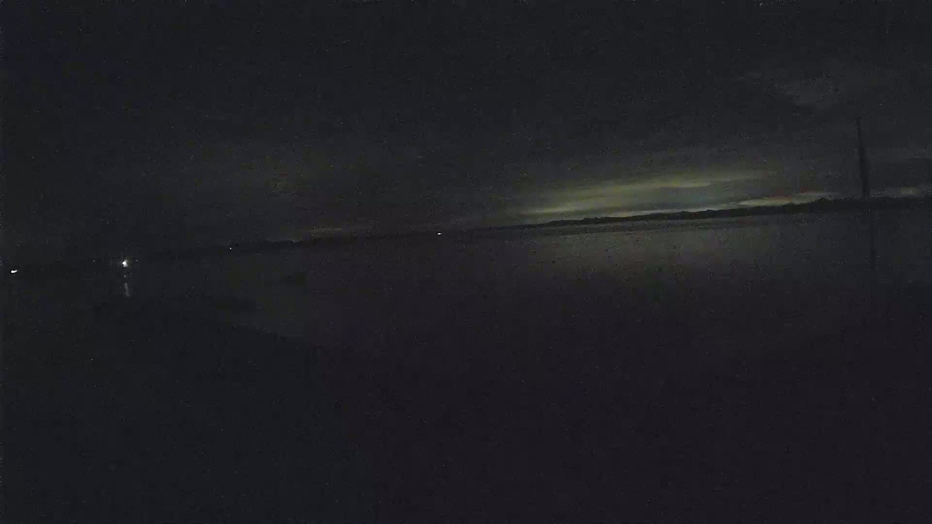 A dark, nighttime view of a calm body of water under a slightly cloudy sky.