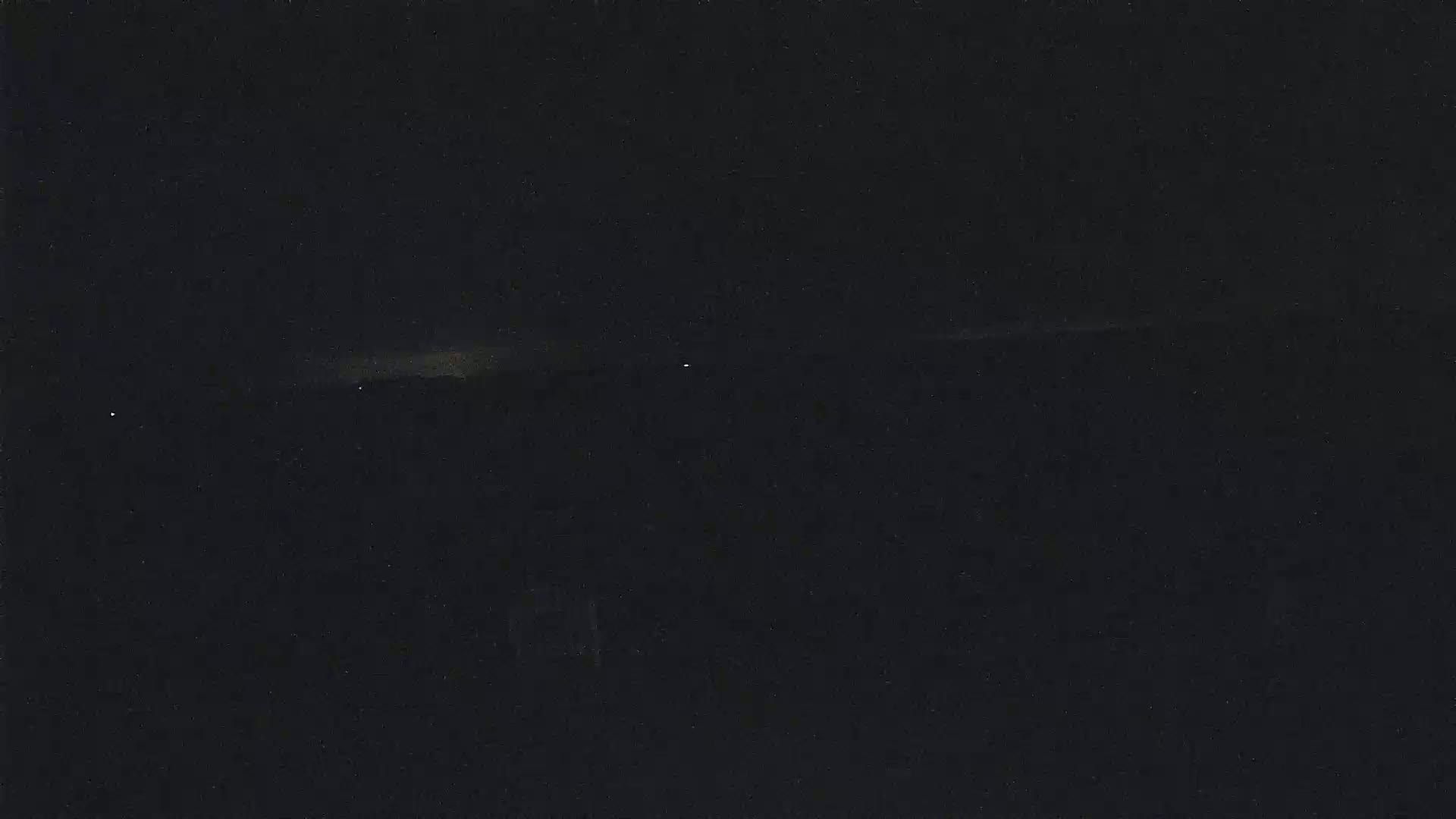 A dark, nighttime landscape is visible, with a faint, light horizon line and a few distant, small lights.