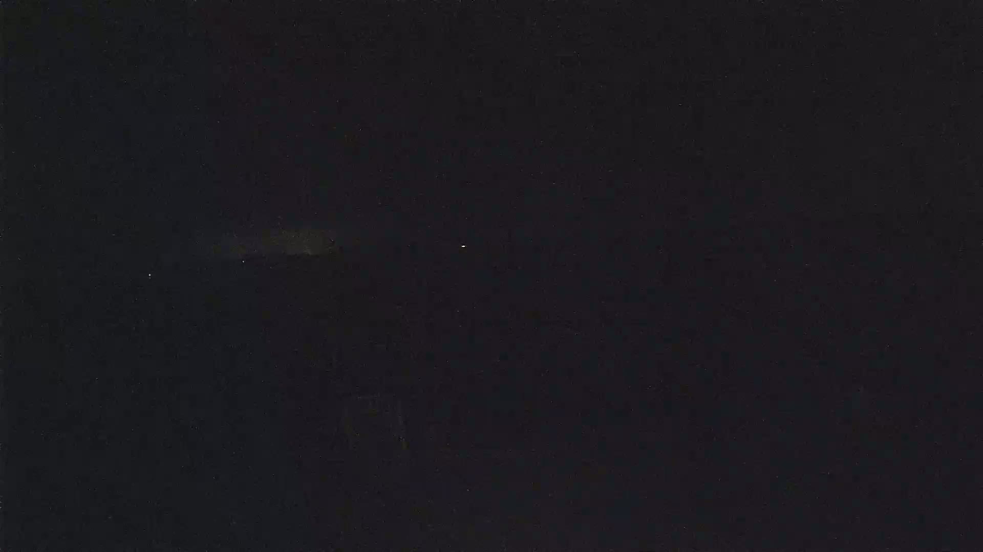 A dark, nighttime scene shows a dimly lit horizon with a few faint lights visible in the distance.