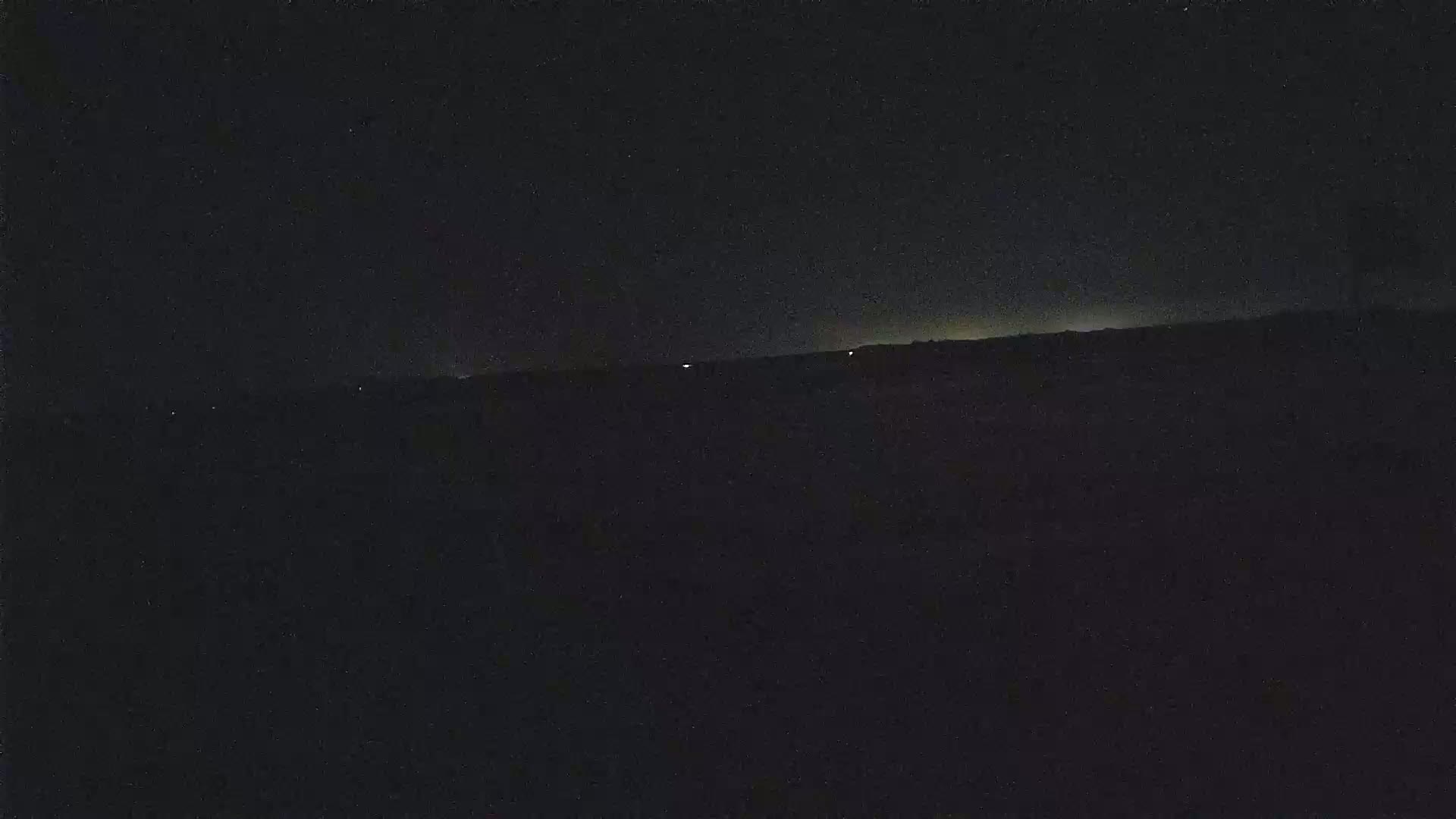 A dark, nighttime landscape shows a distant horizon line with a few faint lights visible.