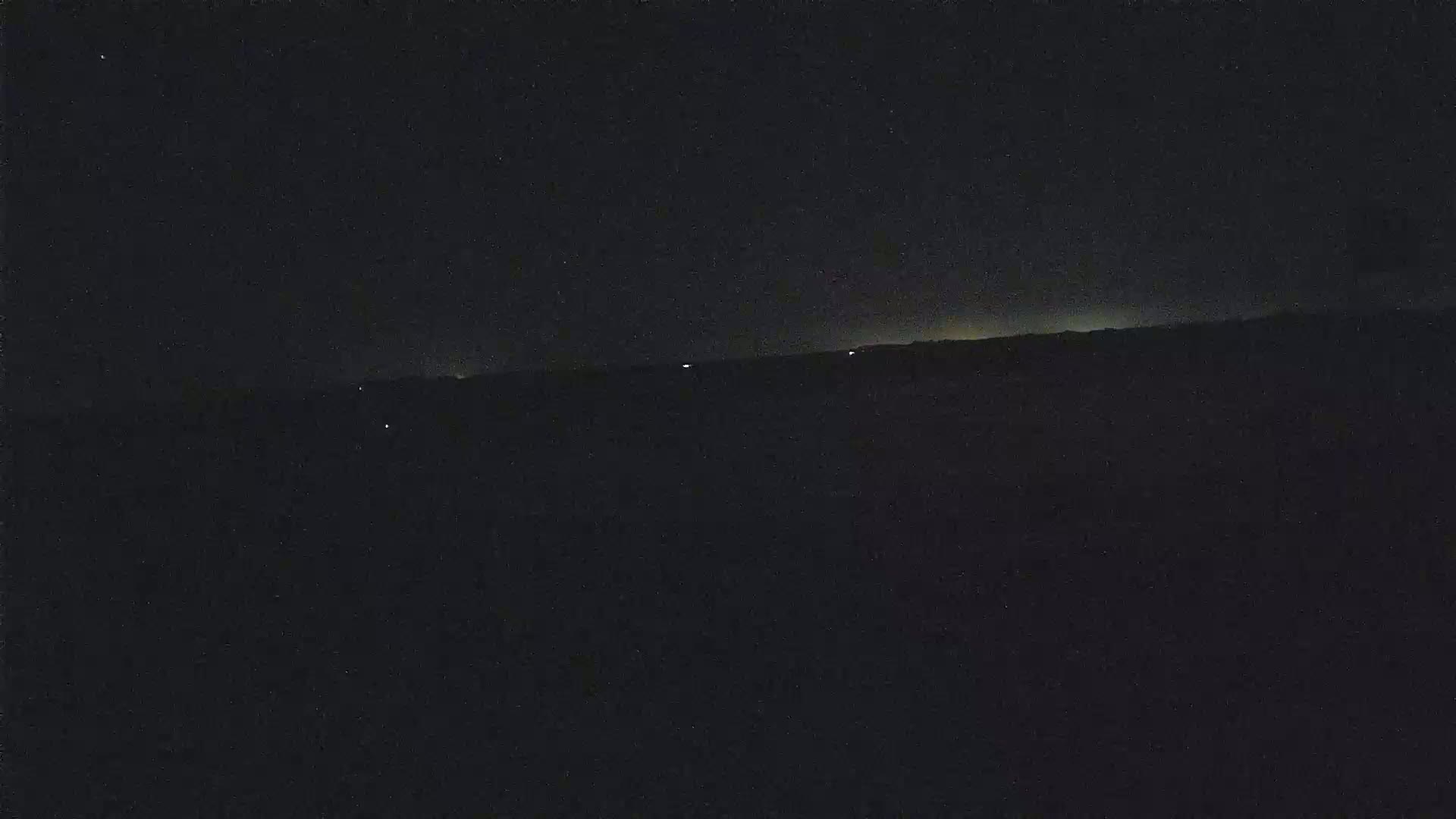 A dark, nighttime landscape is shown with a faint, distant horizon illuminated by a few lights.