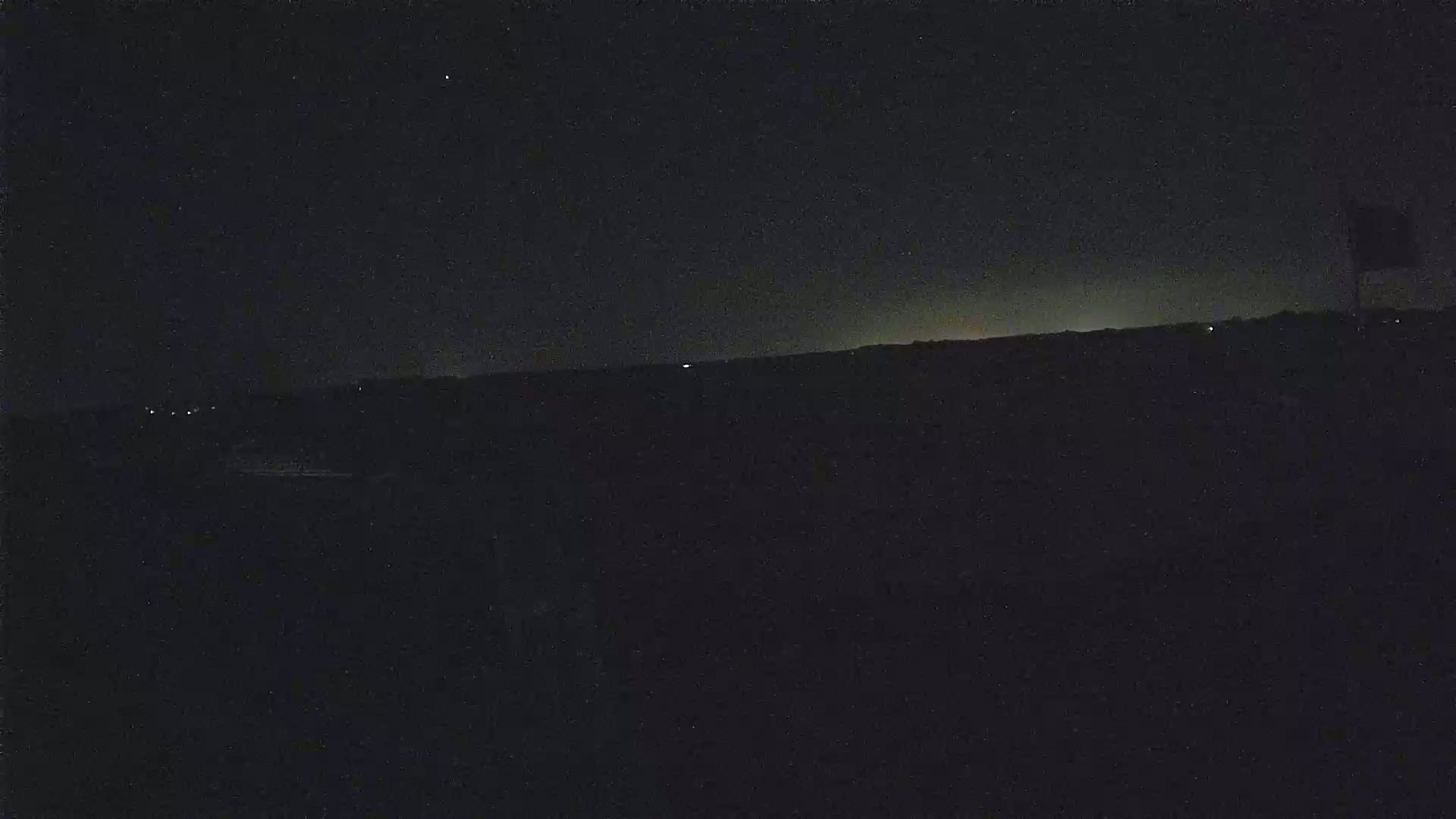 A dark, nighttime landscape is visible, with a faint horizon glow and a few distant lights.