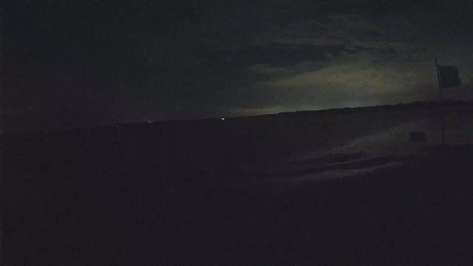 A dark, nighttime landscape with a faintly illuminated horizon under a cloudy sky.