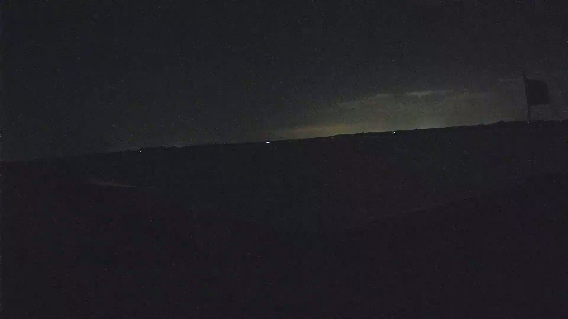 A dark, nighttime landscape is visible with a faintly lit horizon and a single flagpole in the distance.