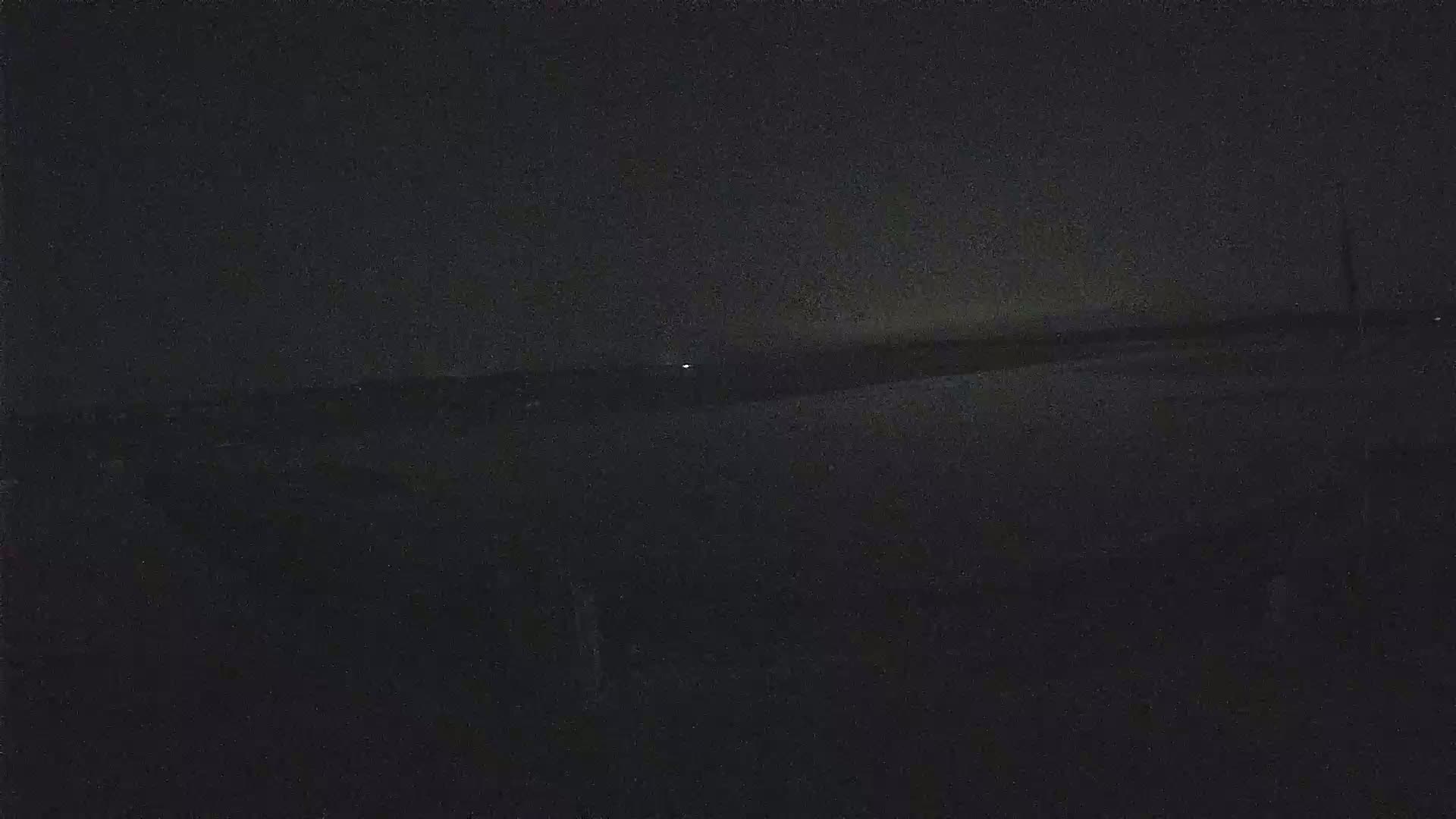 A dark, nighttime scene shows a flat, dark landscape under a mostly clear sky.
