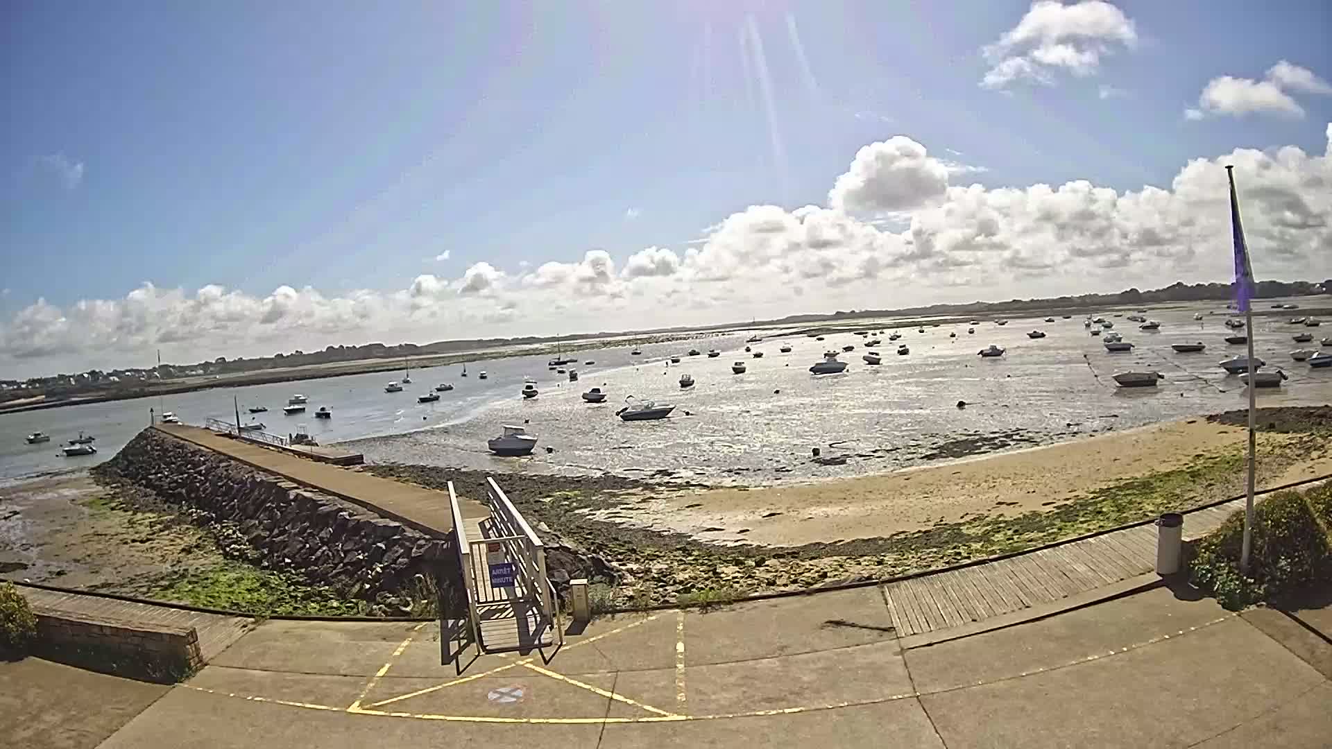 A sandy beach with numerous small boats in shallow water under a partly cloudy sunny sky.