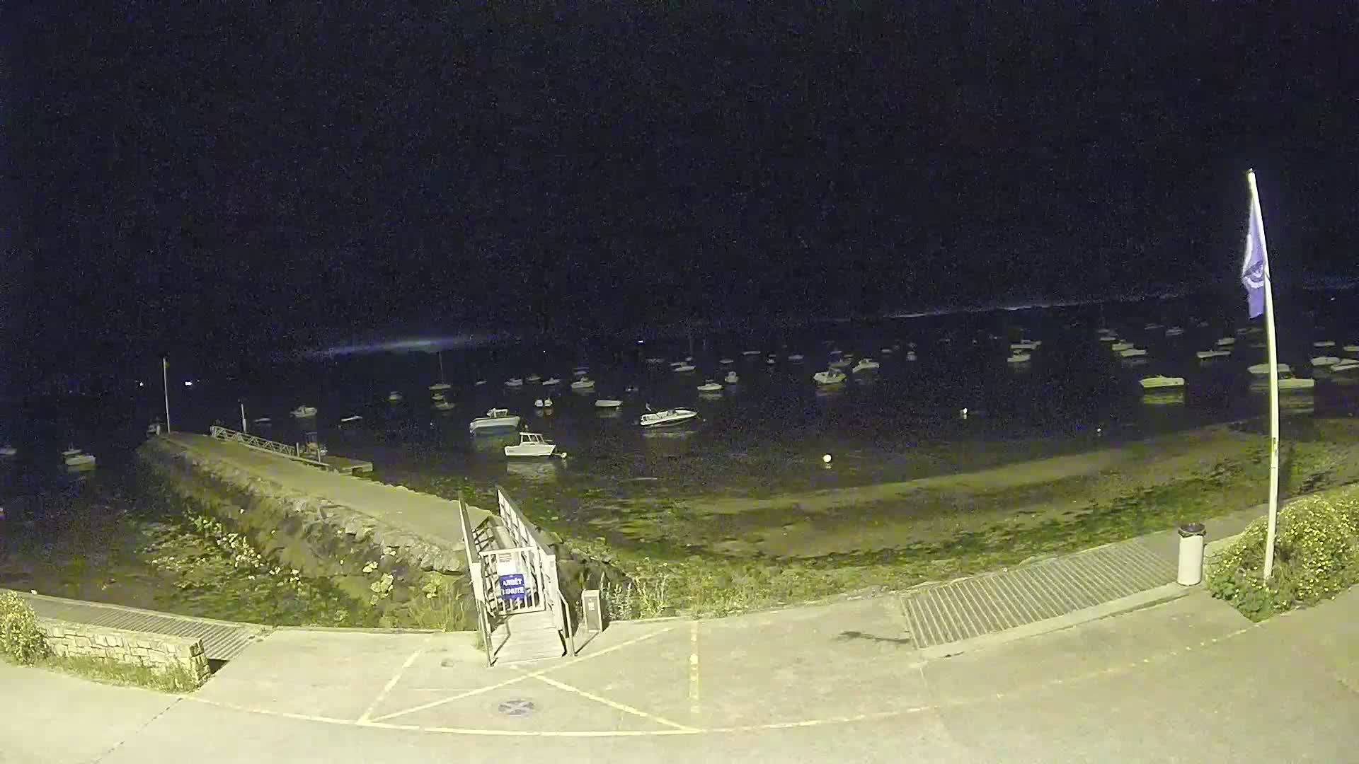 At night, a small harbor is filled with numerous boats at low tide, under a dark, clear sky.