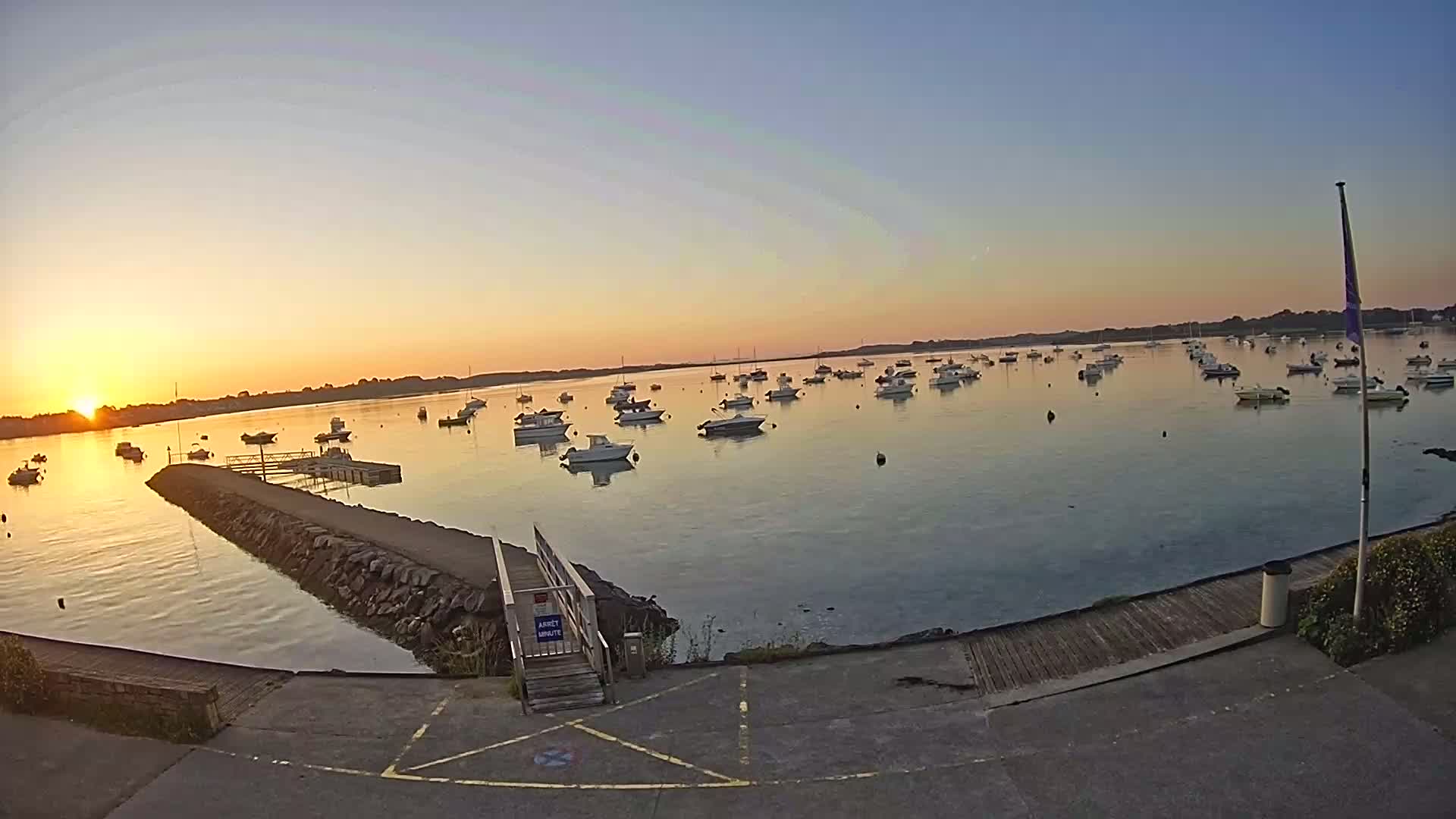 Many small boats are moored in a calm bay at sunrise.