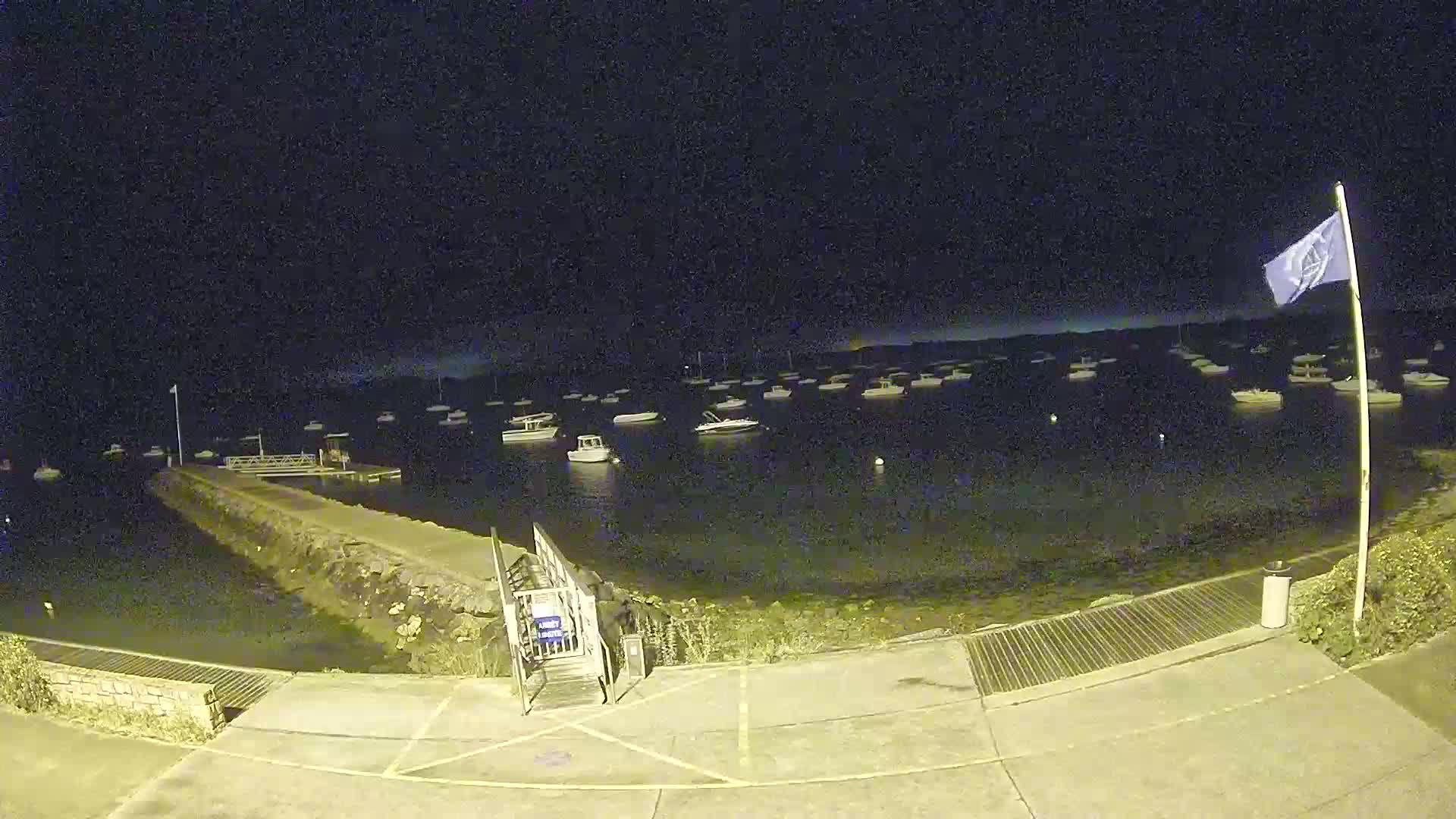 A nighttime view of a harbor with numerous boats at anchor under a clear, dark sky.