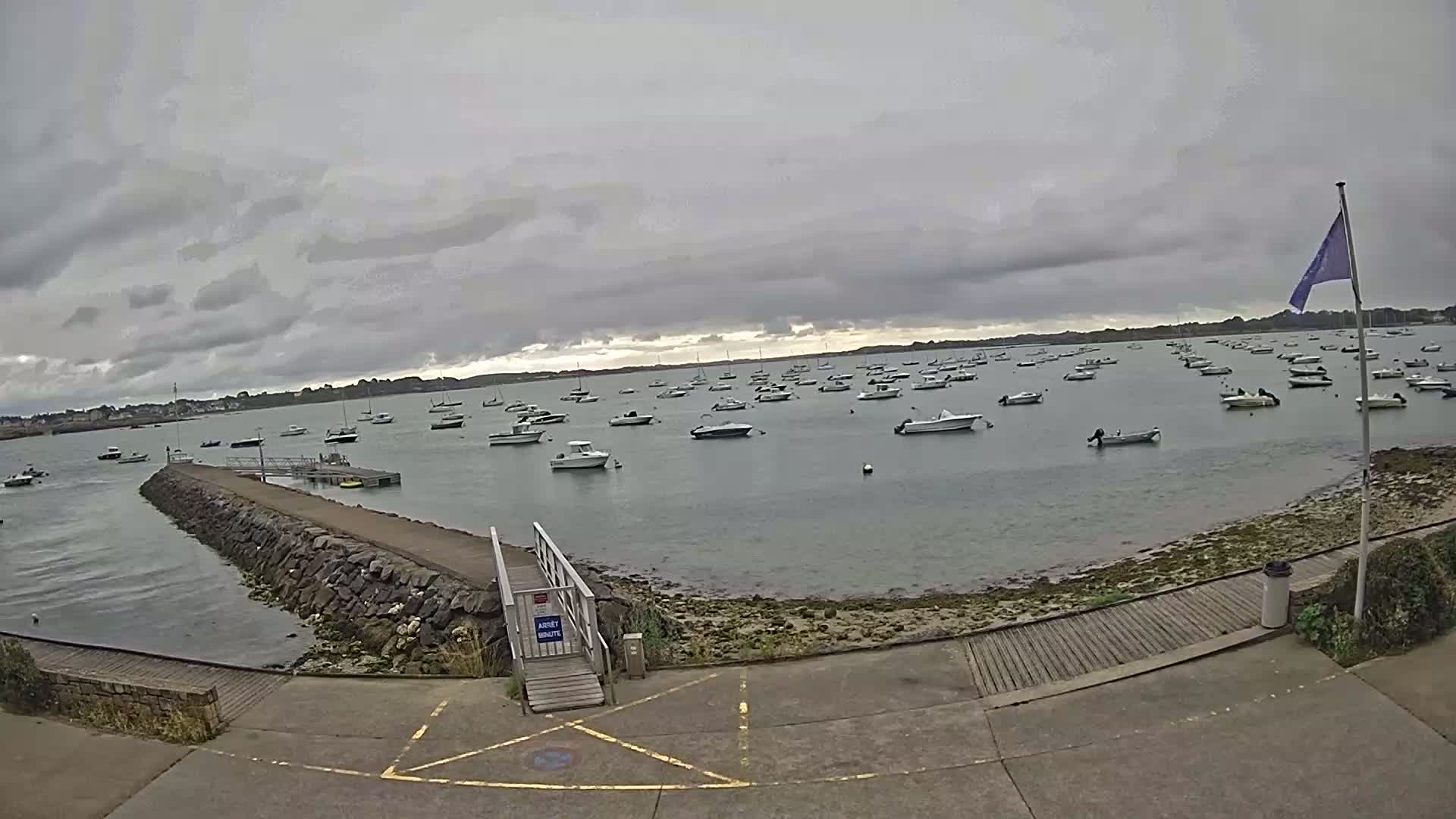 A calm bay with numerous small boats at anchor under an overcast sky.