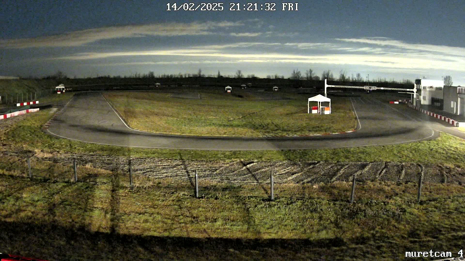 An empty asphalt race track at night under a cloudy sky.