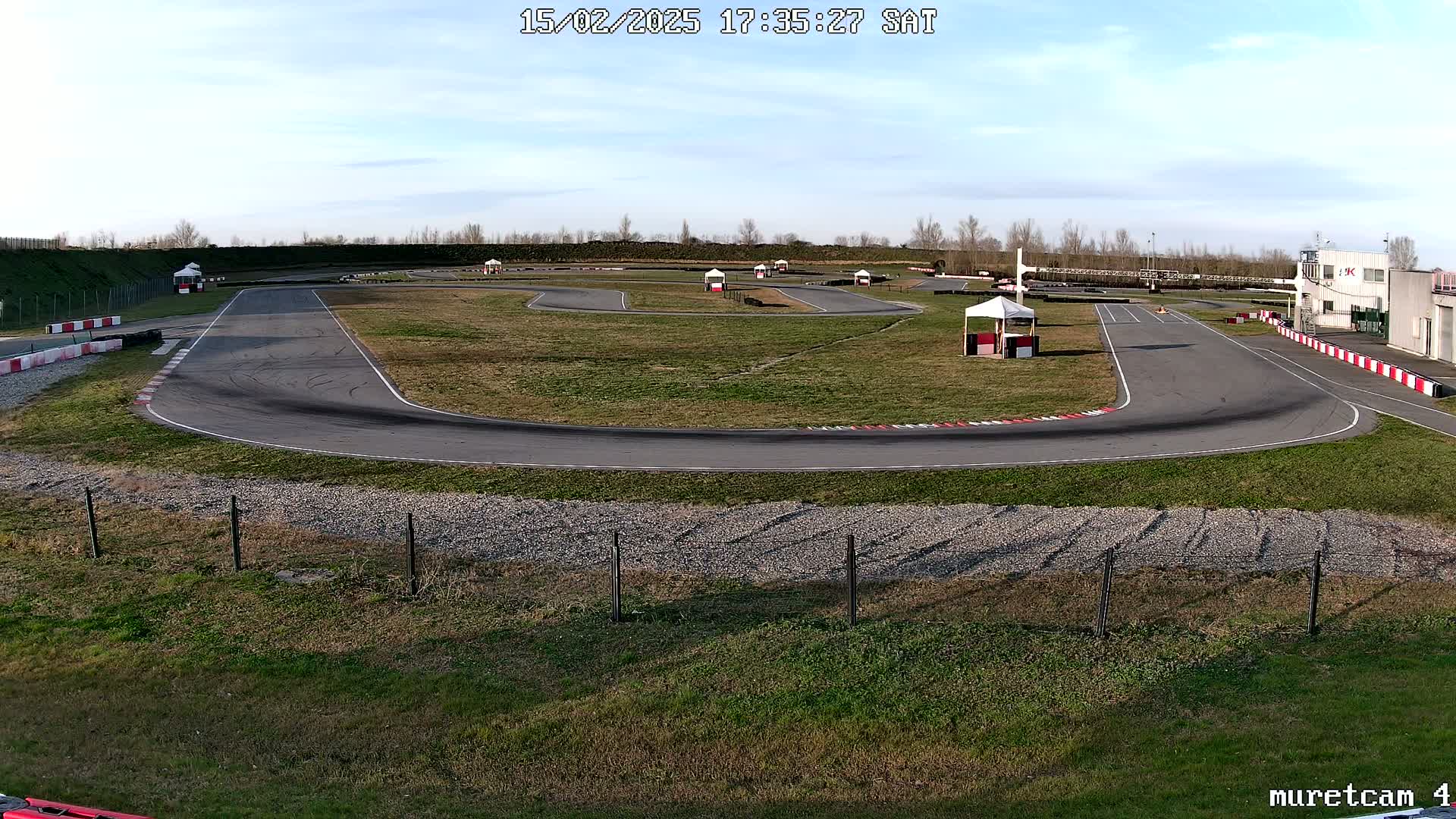 An outdoor go-kart track on a partly sunny day shows tire marks on the asphalt.