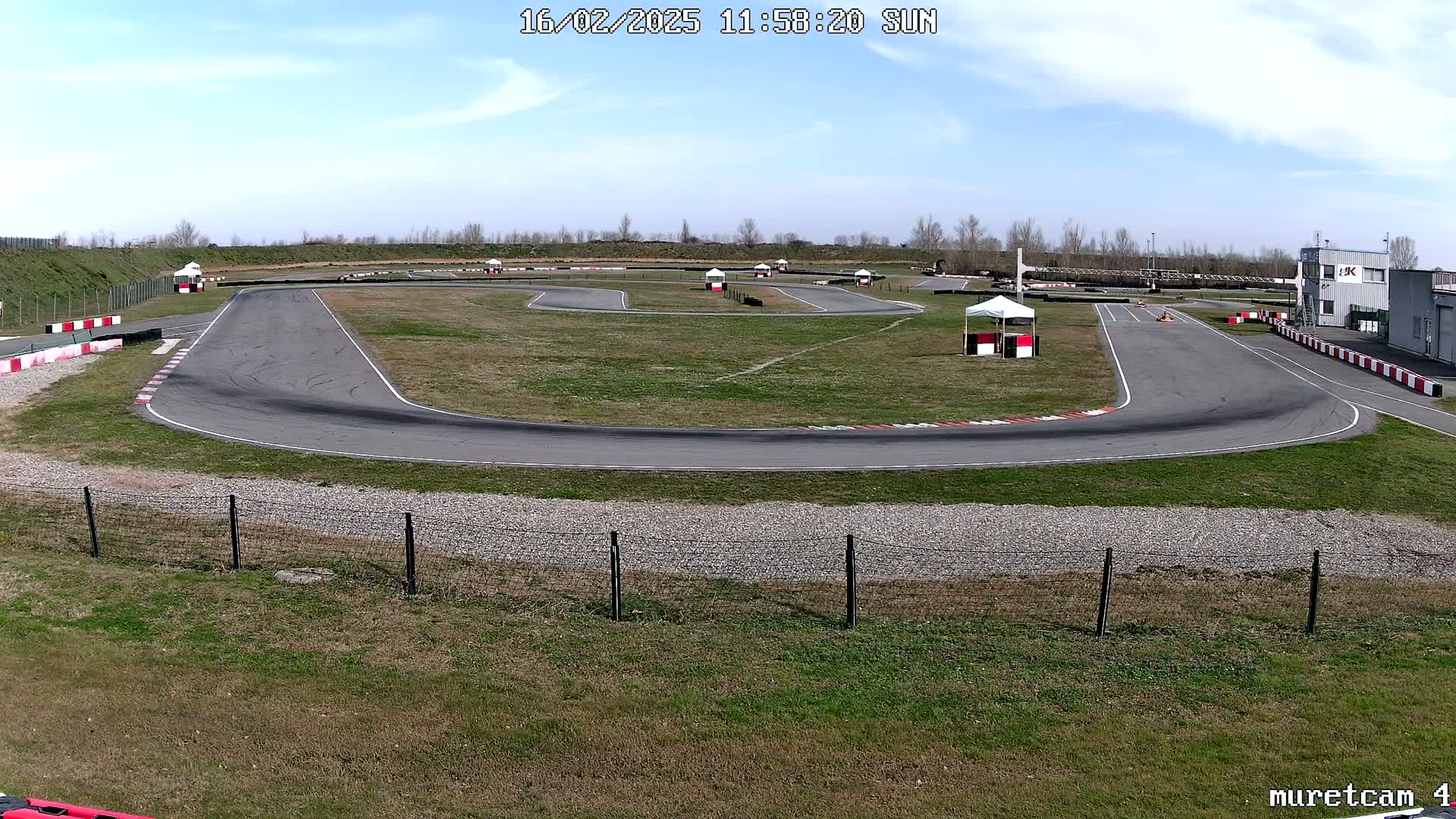 A go-kart track with a paved surface winds through a grassy area under a mostly sunny sky.