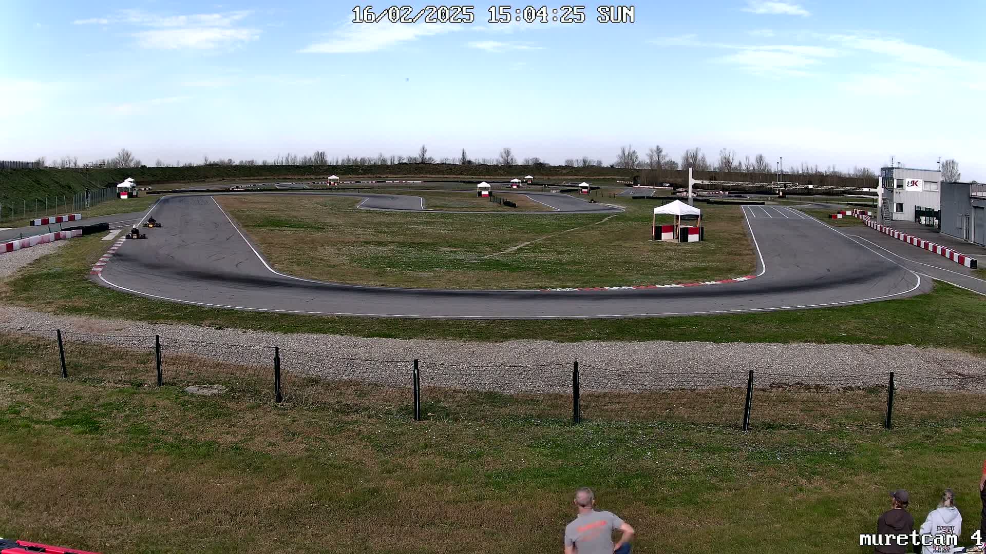 A go-kart track with a few karts on it, under a mostly sunny sky.