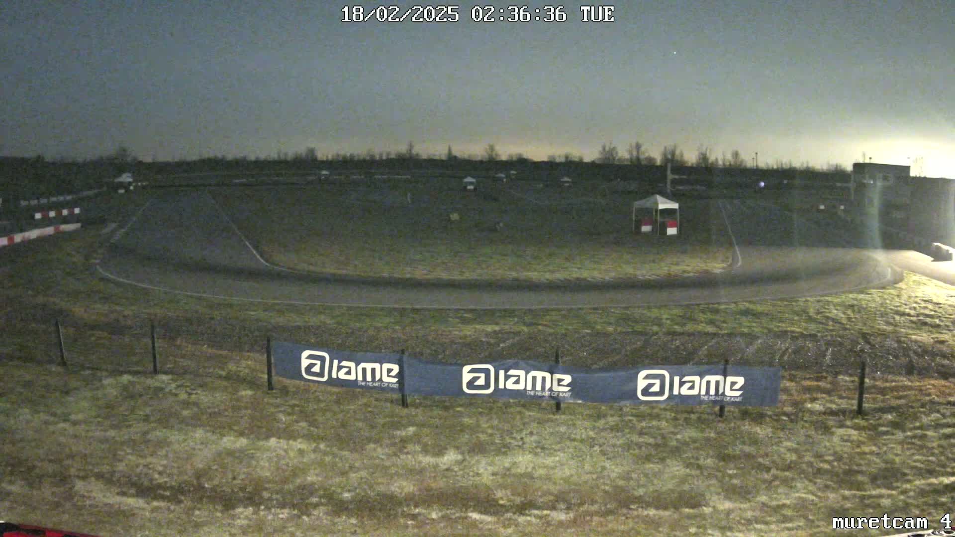 A dimly lit outdoor go-kart track is mostly empty under a dark, overcast sky.
