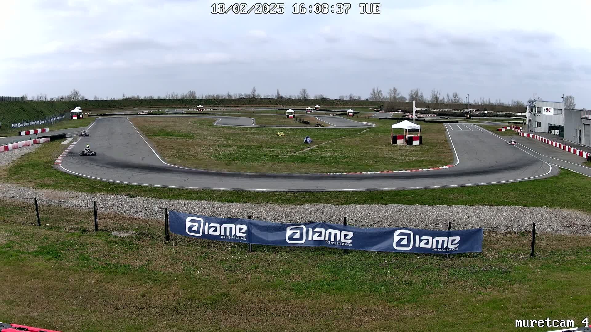 Two go-karts race around a paved outdoor track on an overcast day.