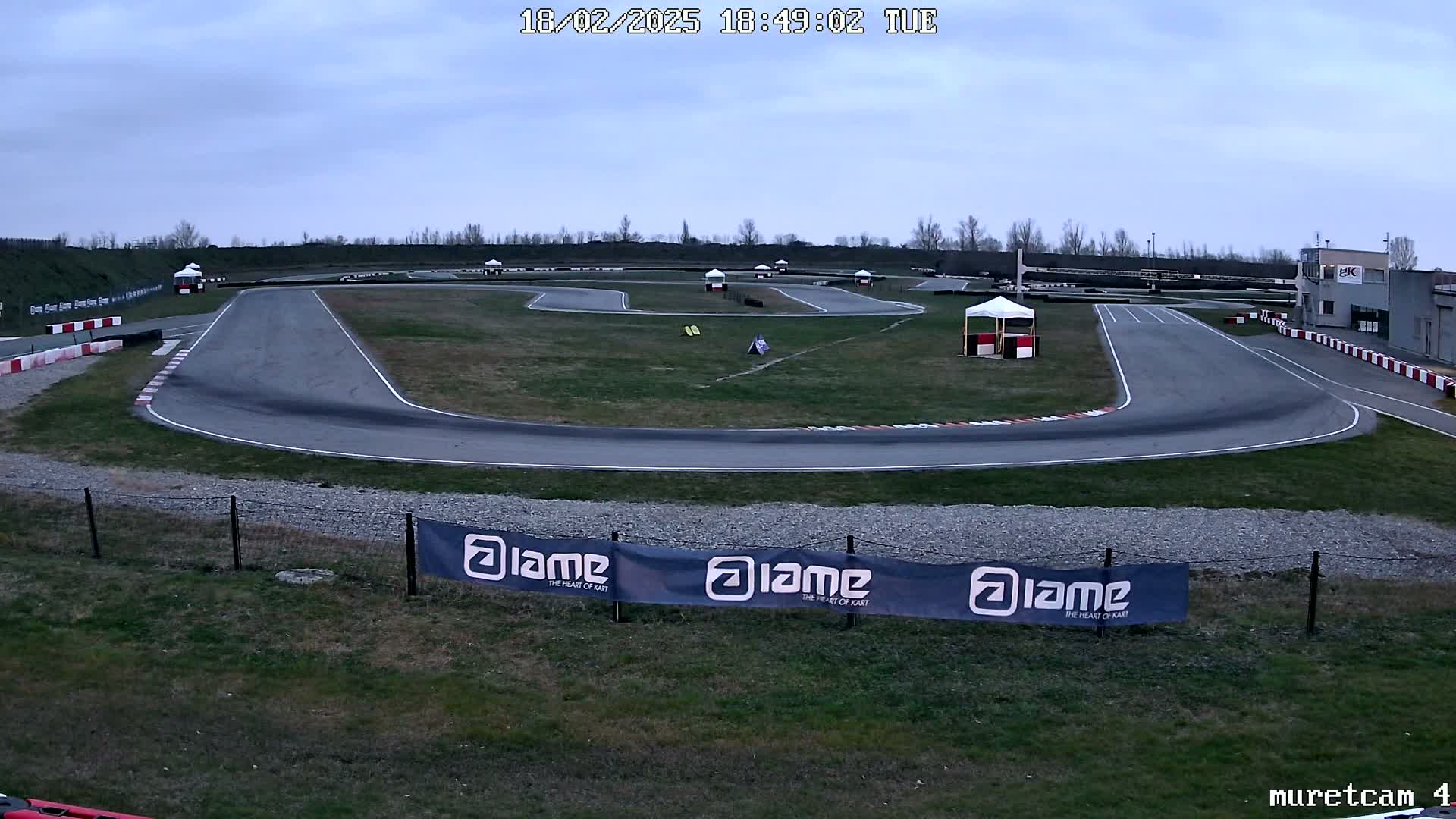 An outdoor go-kart track under a cloudy sky, showing a paved course winding through a grassy area.