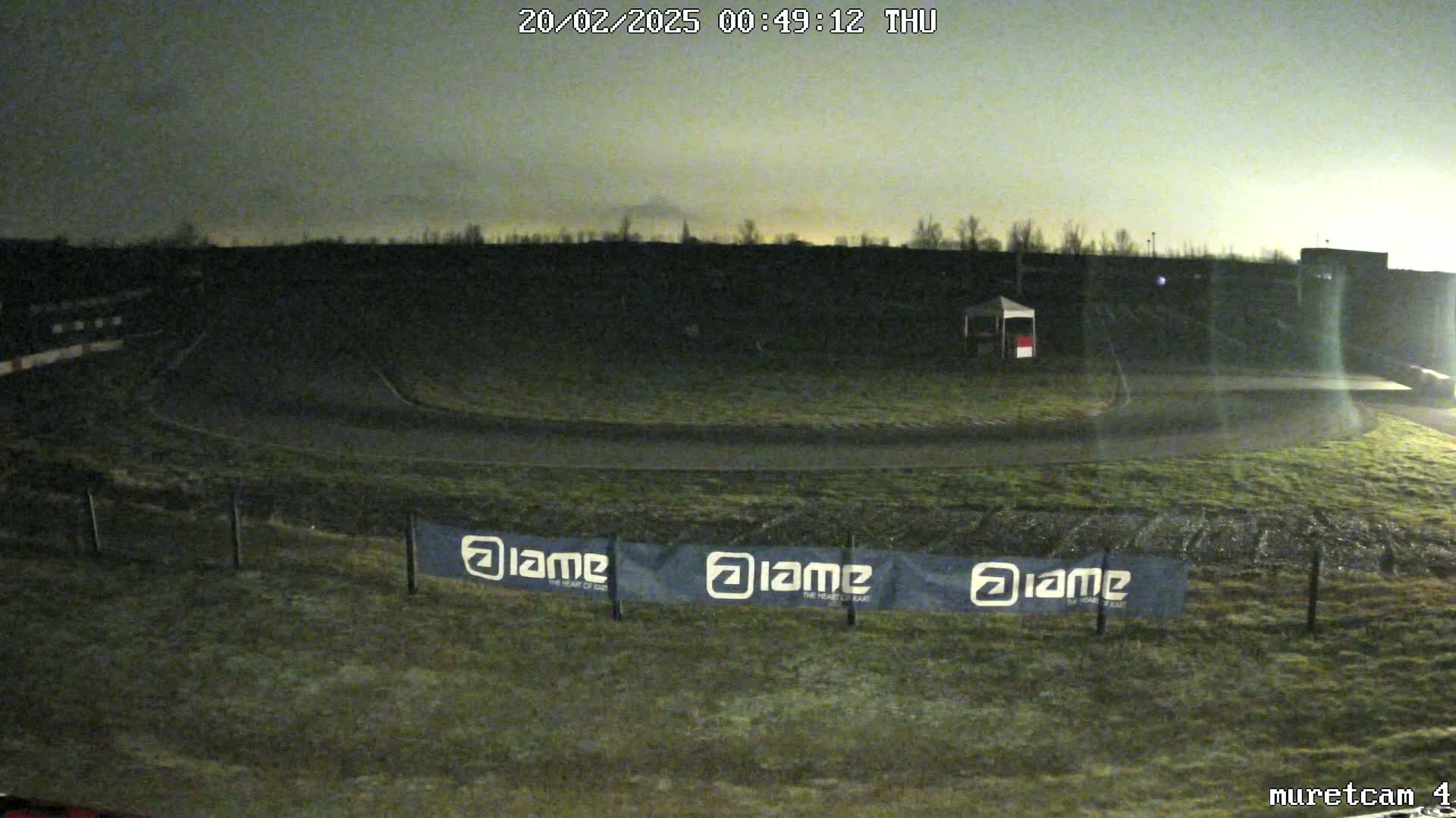 A nighttime view of a dark, grassy racetrack under a cloudy sky.