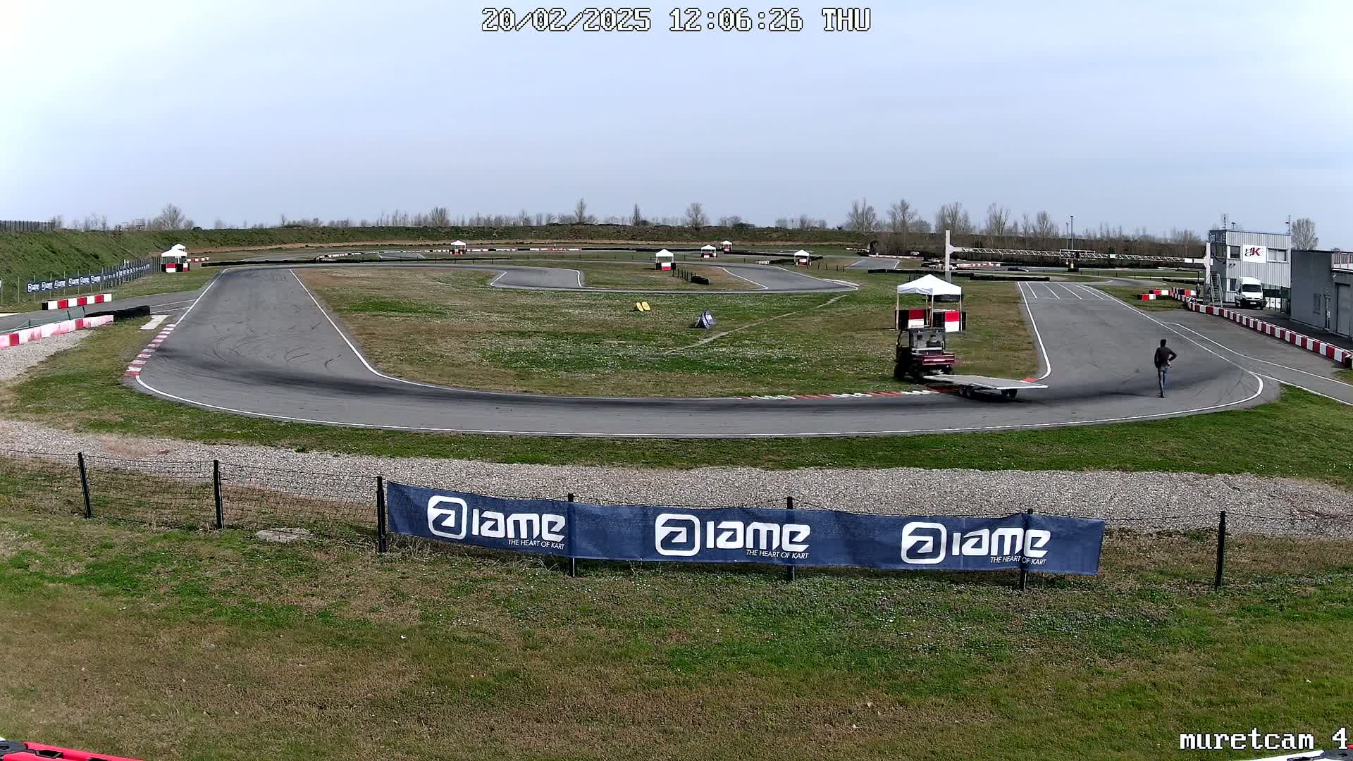 A go-kart track with a person walking on it, under a mostly clear sky.