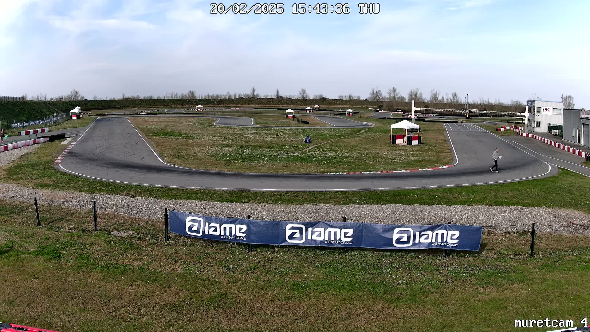 An outdoor go-kart track on a partly sunny day with a person walking near the edge of the track.