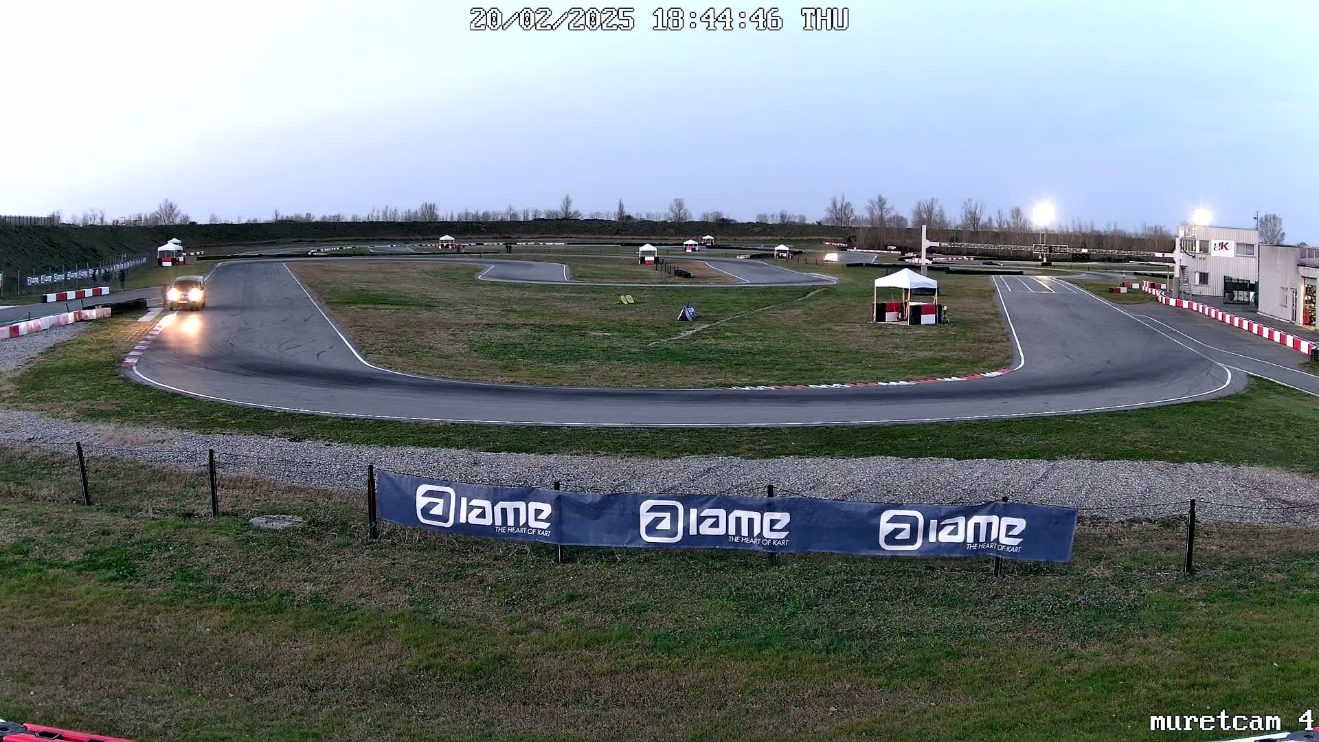 A go-kart is driving on a paved track under a twilight sky.