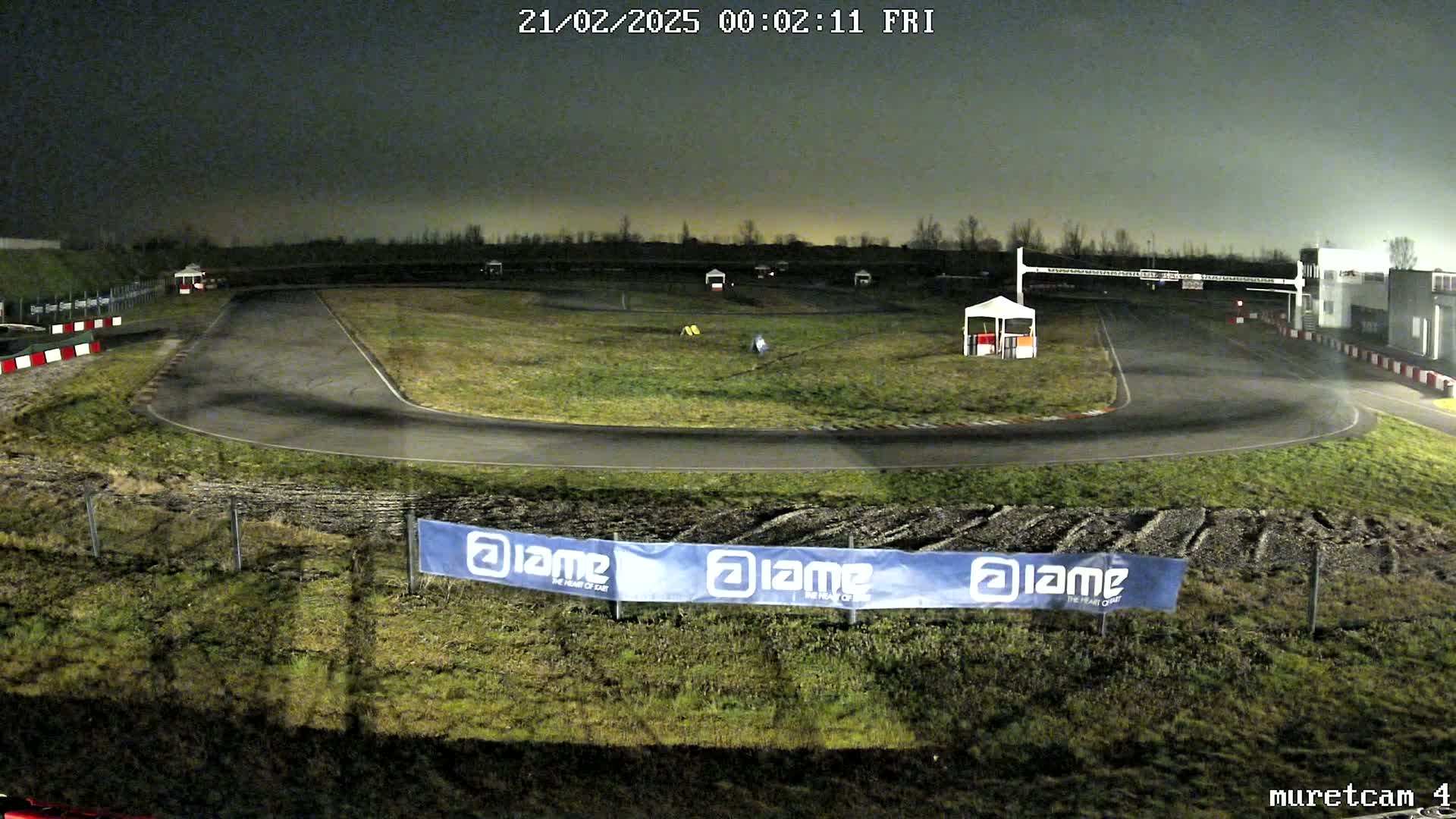 An empty asphalt go-kart track at night under a dark sky is surrounded by patchy grass.