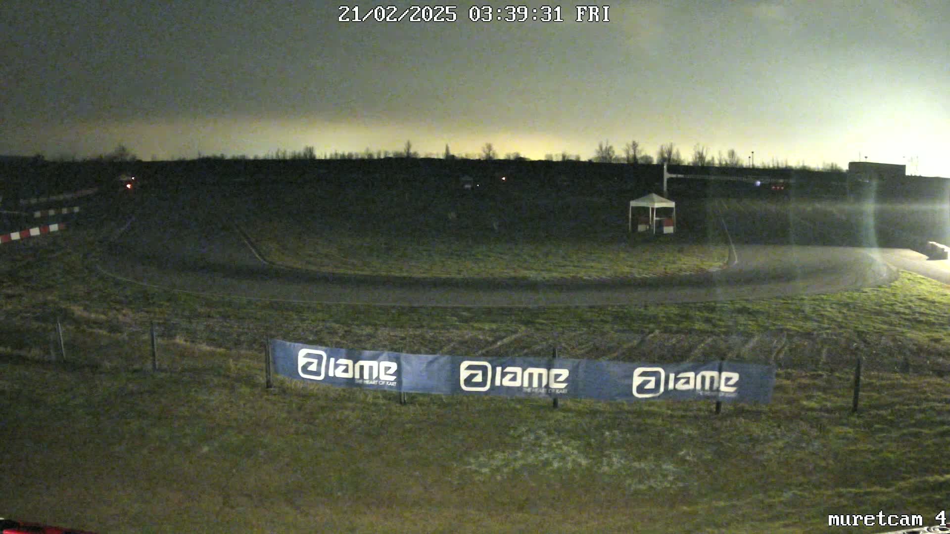 A nighttime view of a dimly lit go-kart track with a small structure and a banner.
