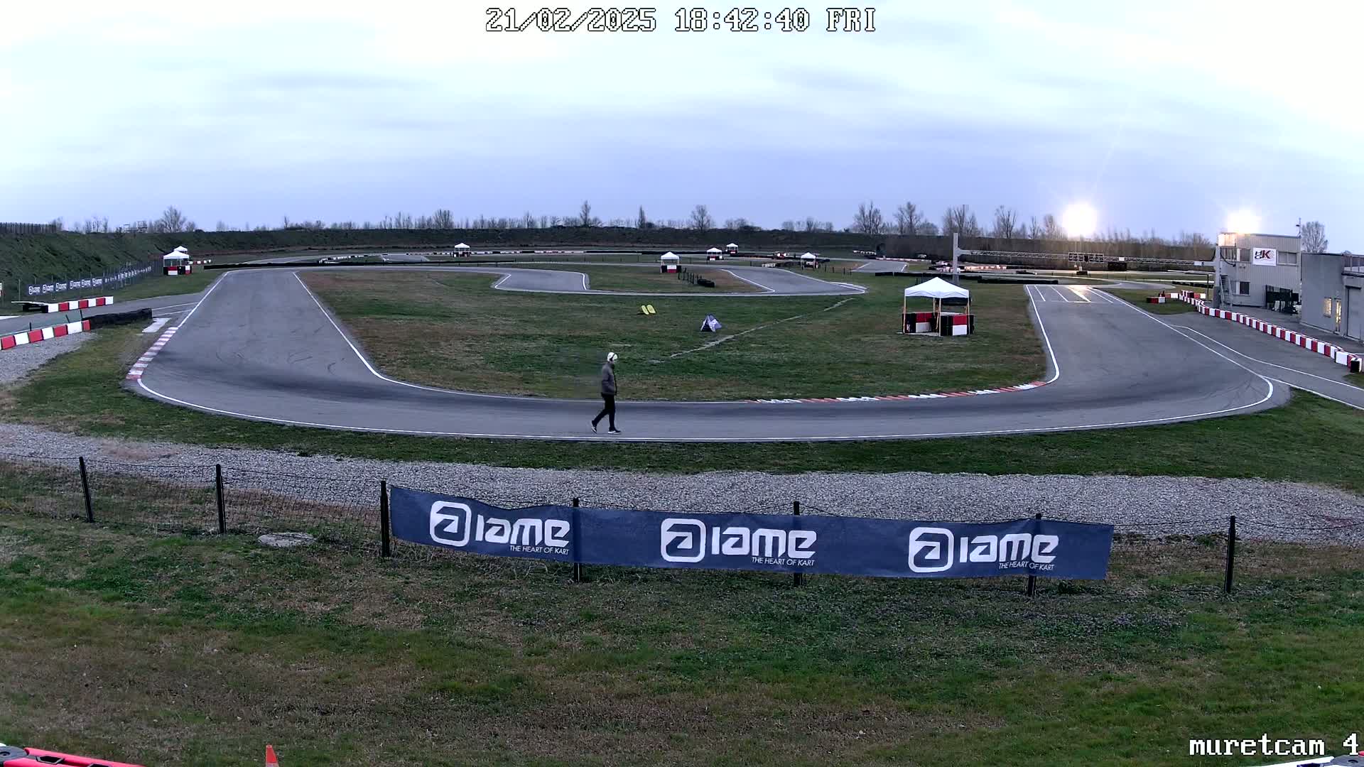 A person walks across a deserted go-kart track under a cloudy twilight sky.