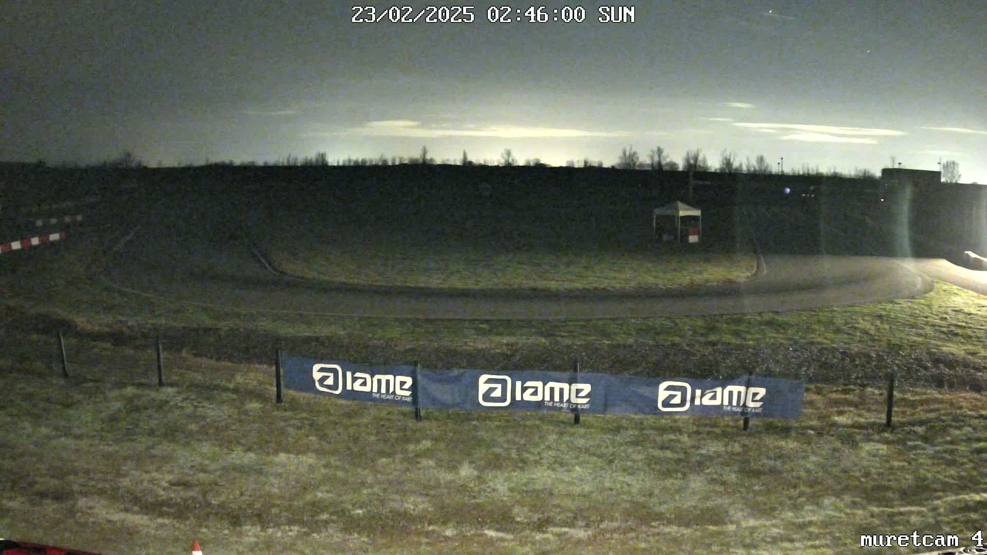 A dimly lit outdoor go-kart track under a dark, mostly cloudy night sky, showing frost on the ground and a few banners along the fence.