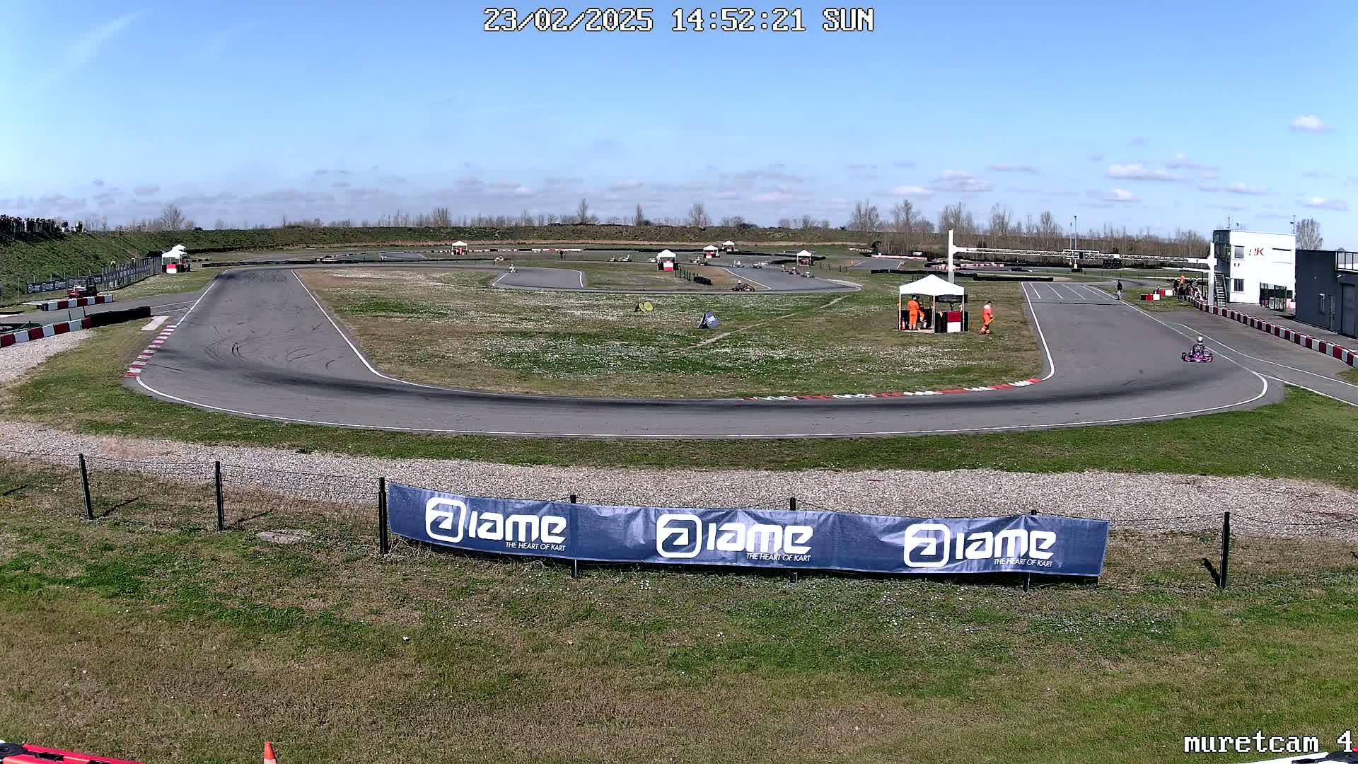 A go-kart track with several go-karts and people visible under a sunny sky.