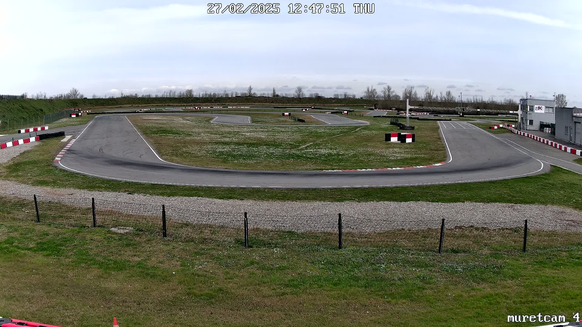 An outdoor go-kart track with a mostly cloudy sky is shown, with the track winding through a grassy area.