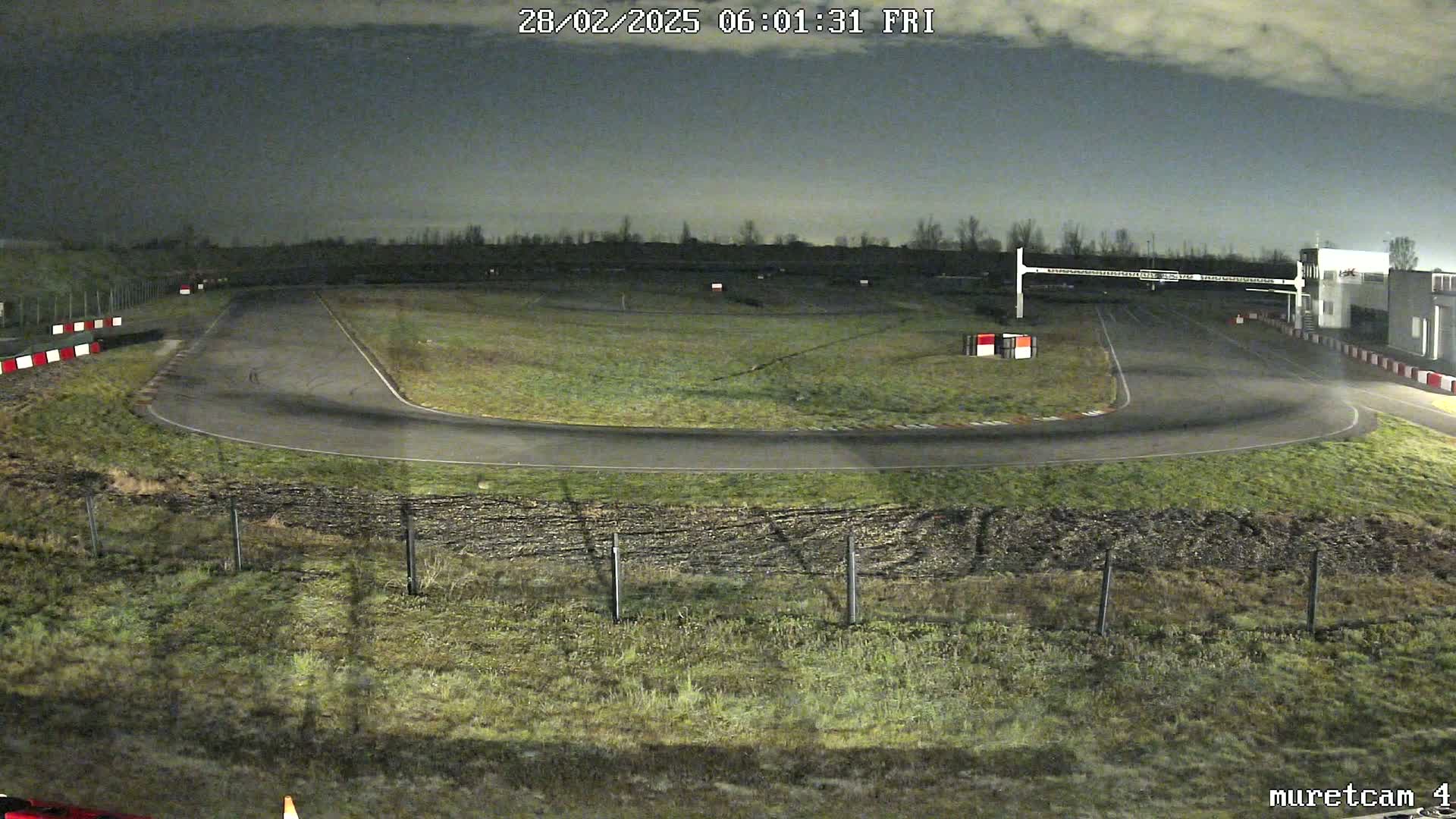 A nighttime view of a paved racetrack curving to the left, surrounded by grassy areas under a cloudy sky.