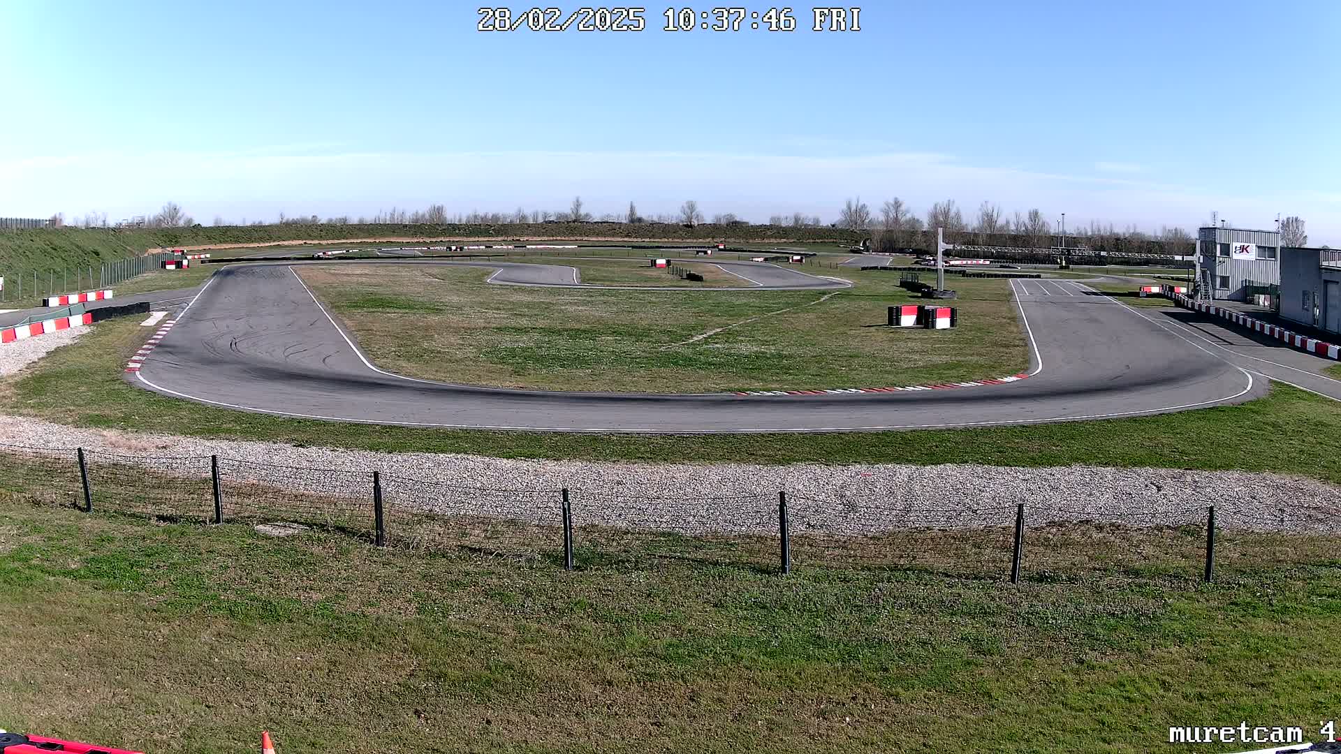 A go-kart track with a paved surface and grassy areas surrounding it under a clear, sunny sky.