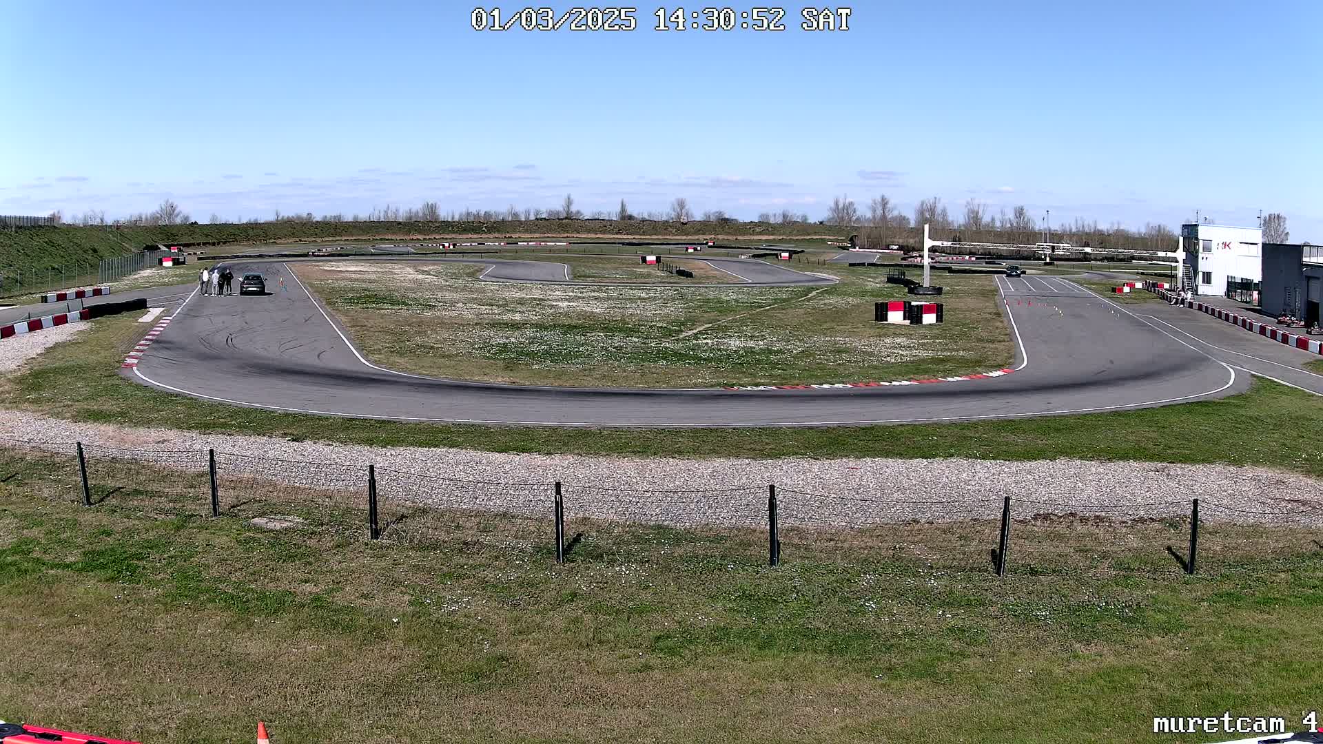 A paved race track with a car and several people standing near it, under a clear blue sky.