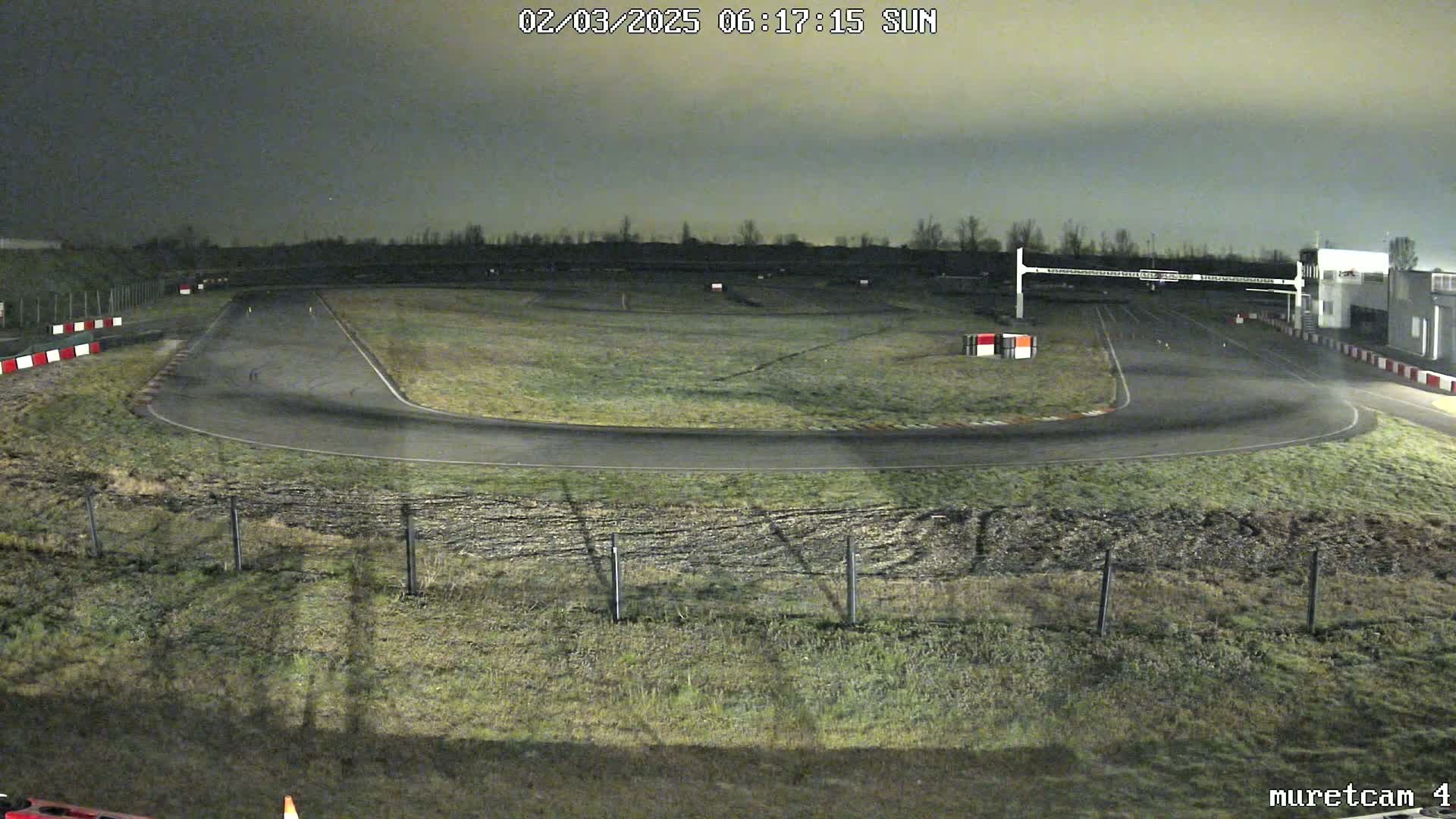 A nighttime, dimly lit view of an empty race track with short grass and sparse trees in the background.