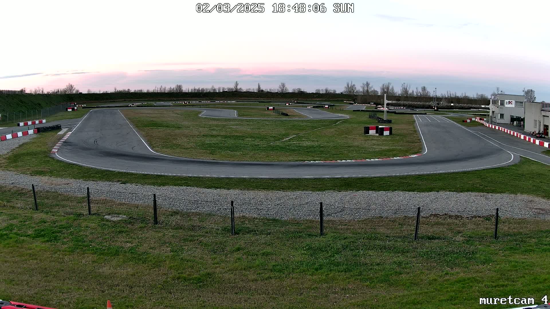 An empty asphalt go-kart track with a grassy infield is shown under a twilight sky.