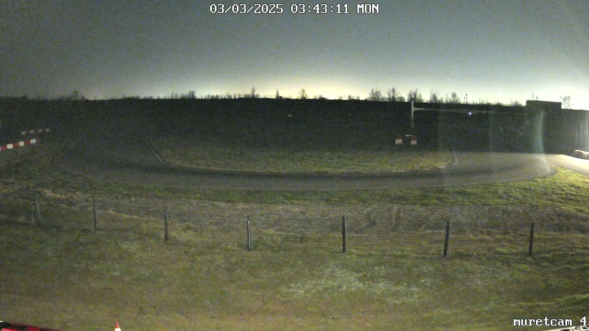 A nighttime view of a paved roadway curving around a grassy area, under a dark sky.