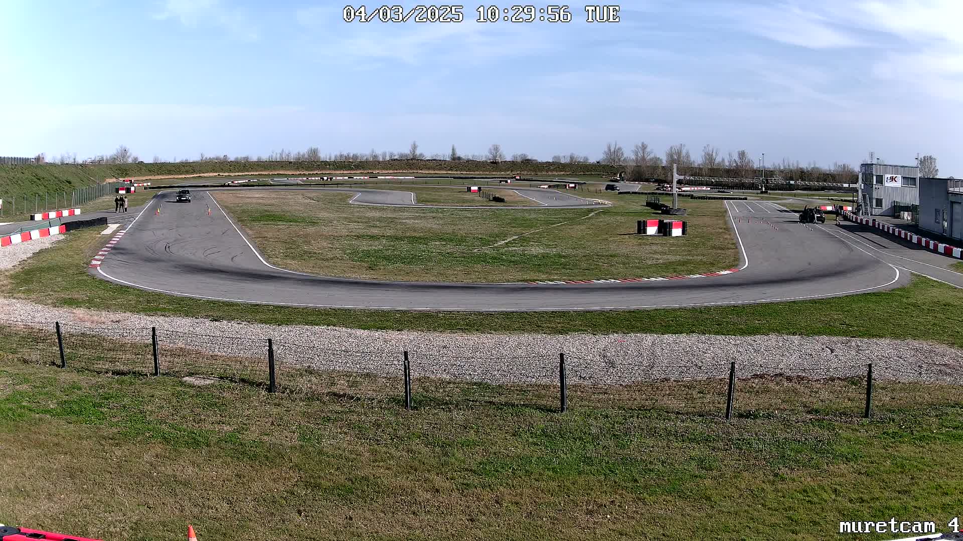 A paved racetrack with a few vehicles and people on a sunny day.
