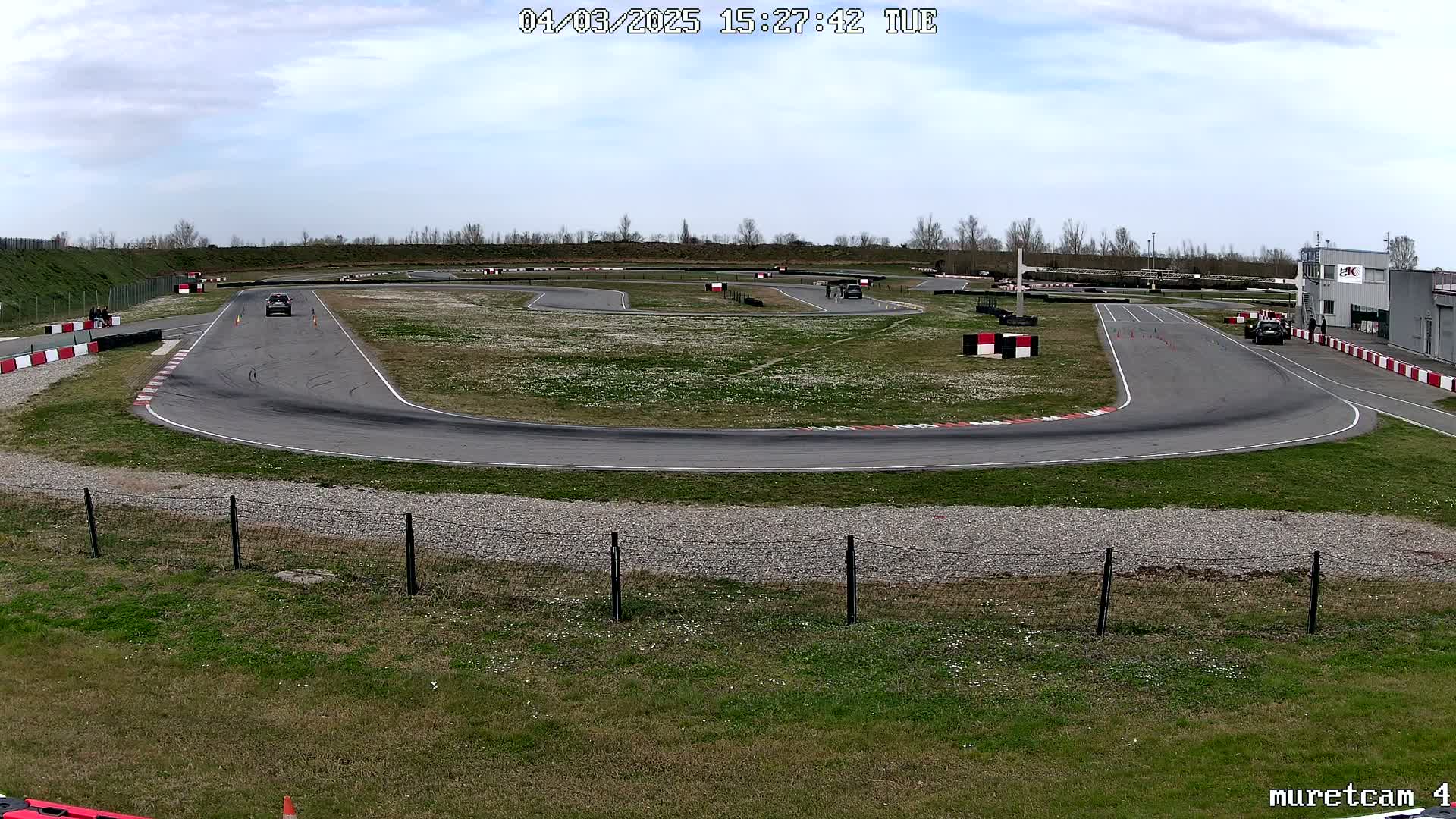 A paved autocross course with several cars and people present under a partly cloudy sky.