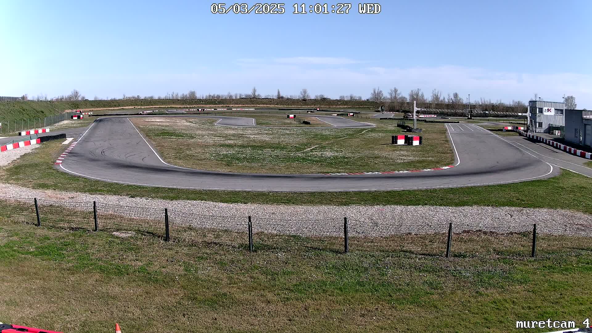 An empty asphalt go-kart track with red and white barriers winds through a grassy area under a clear blue sky.