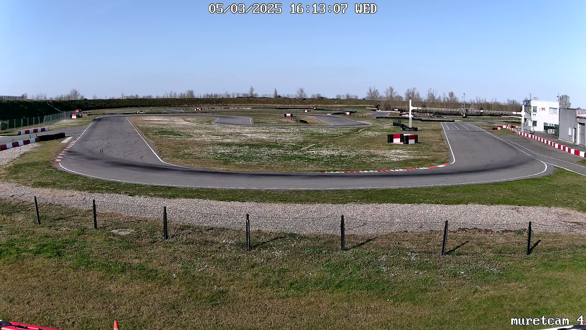 An empty asphalt go-kart track winds through a grassy field under a clear blue sky.