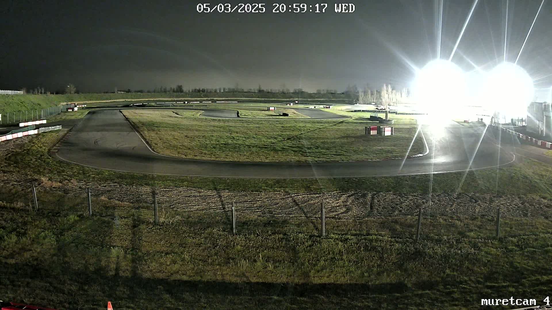 A nighttime view of a brightly lit go-kart track with short grass surrounding it.