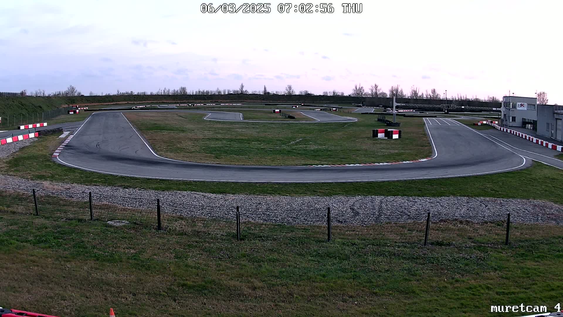 An empty go-kart track with overcast skies is seen from a high vantage point.
