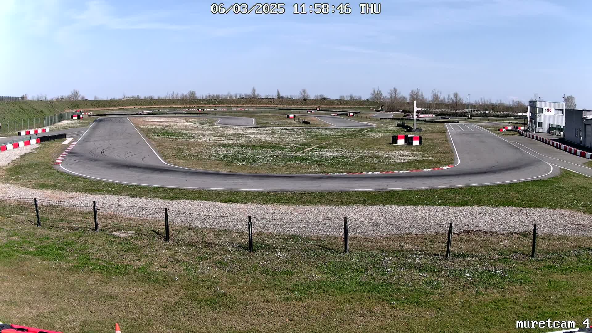 An empty asphalt go-kart track winds through a grassy area under a clear, sunny sky.