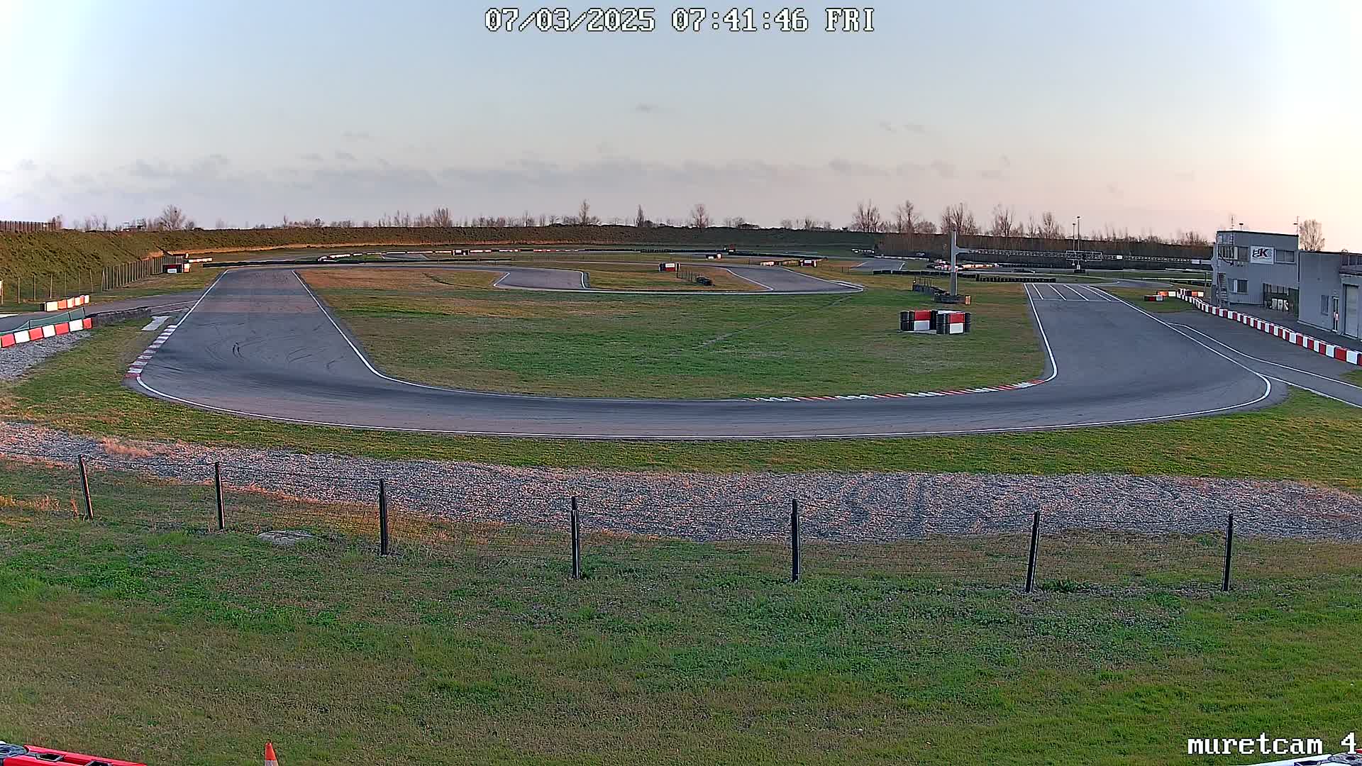 An empty go-kart track with grassy areas and a building is visible under a clear, twilight sky.