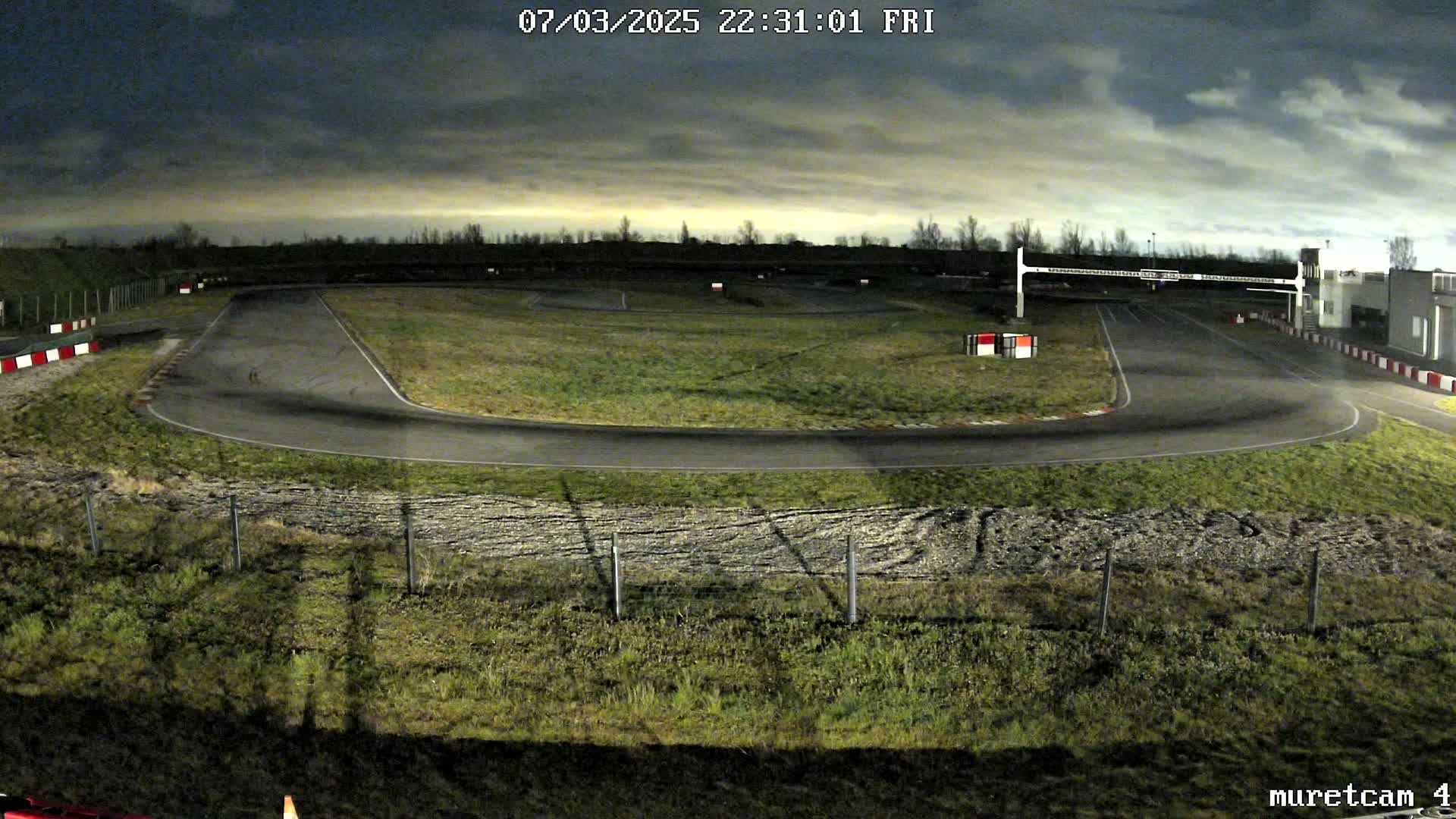 An empty go-kart track at night under a cloudy sky.