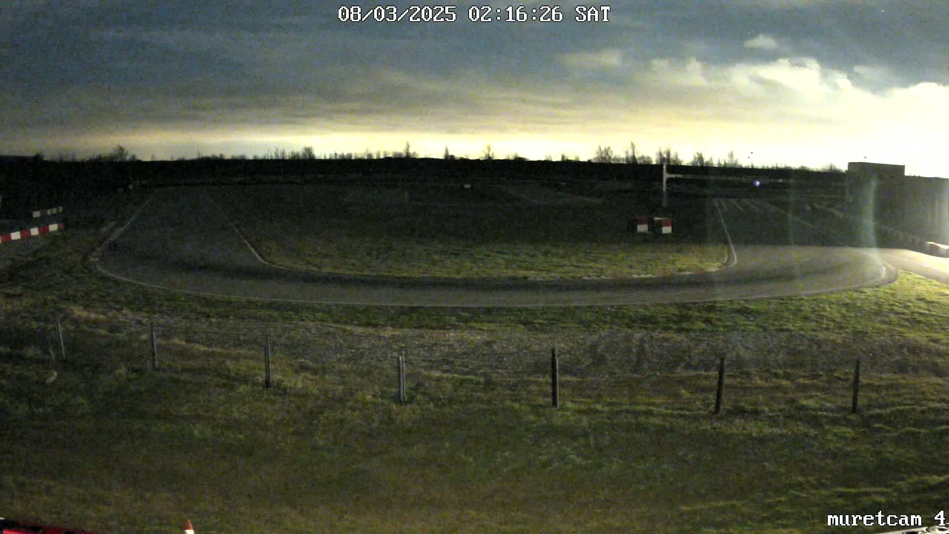 A nighttime view of an empty race track under a cloudy sky.