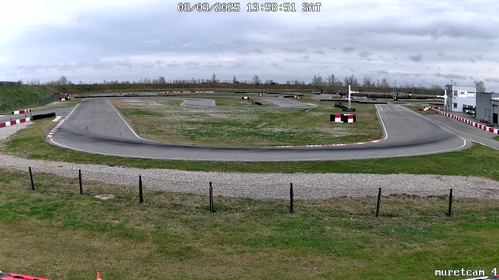 An outdoor go-kart track with a paved surface and grassy areas, under a partly cloudy sky.