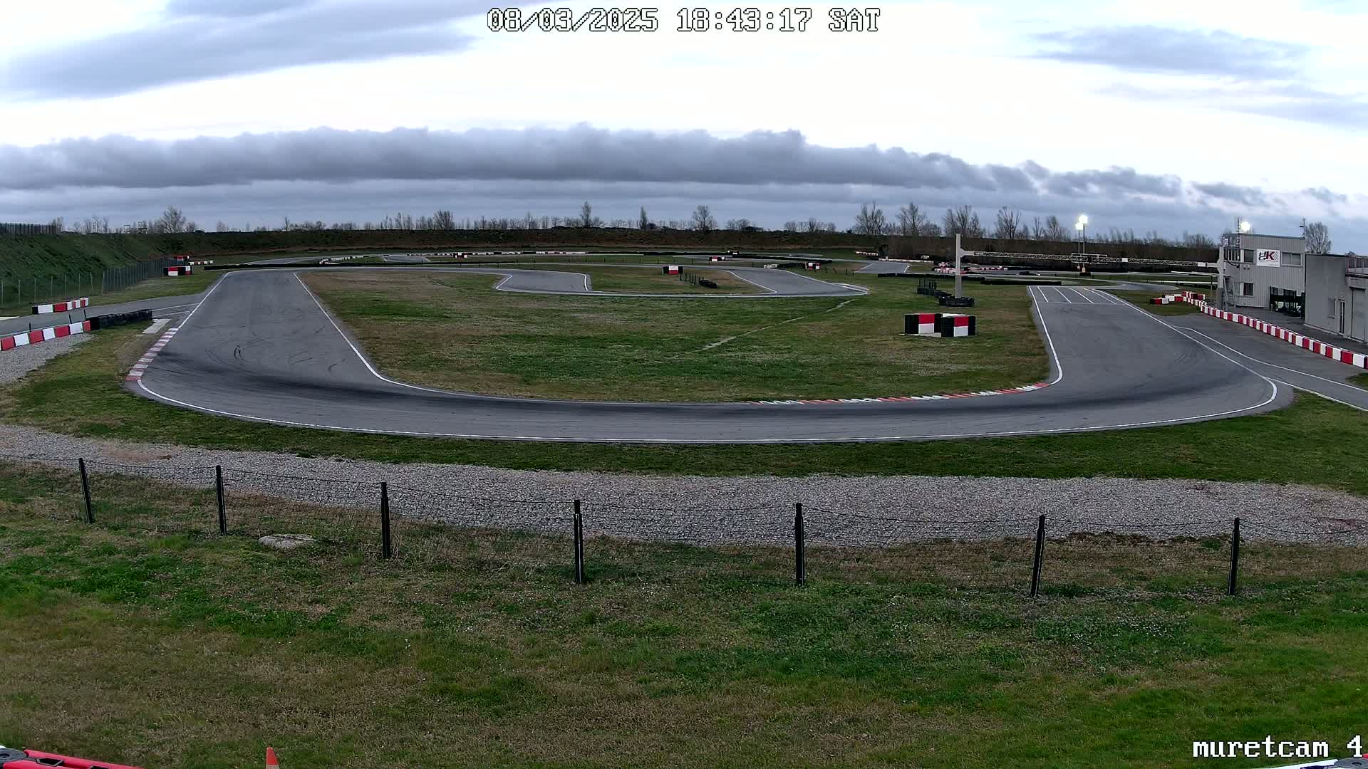 A go-kart track with a paved surface, surrounded by grass under a cloudy sky.