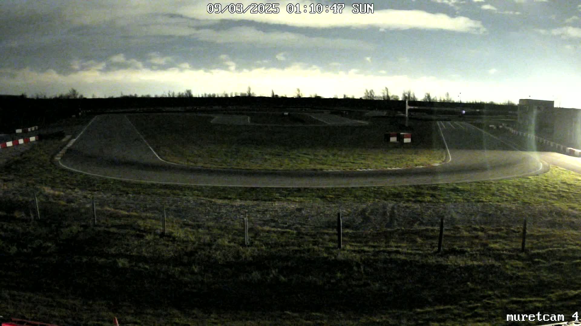 A dimly lit go-kart track under a cloudy night sky.